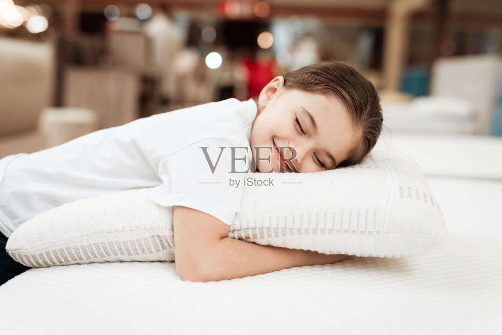 可爱的小女孩拥抱枕头在骨科床垫商店。测试枕头的柔软度。照片摄影图片