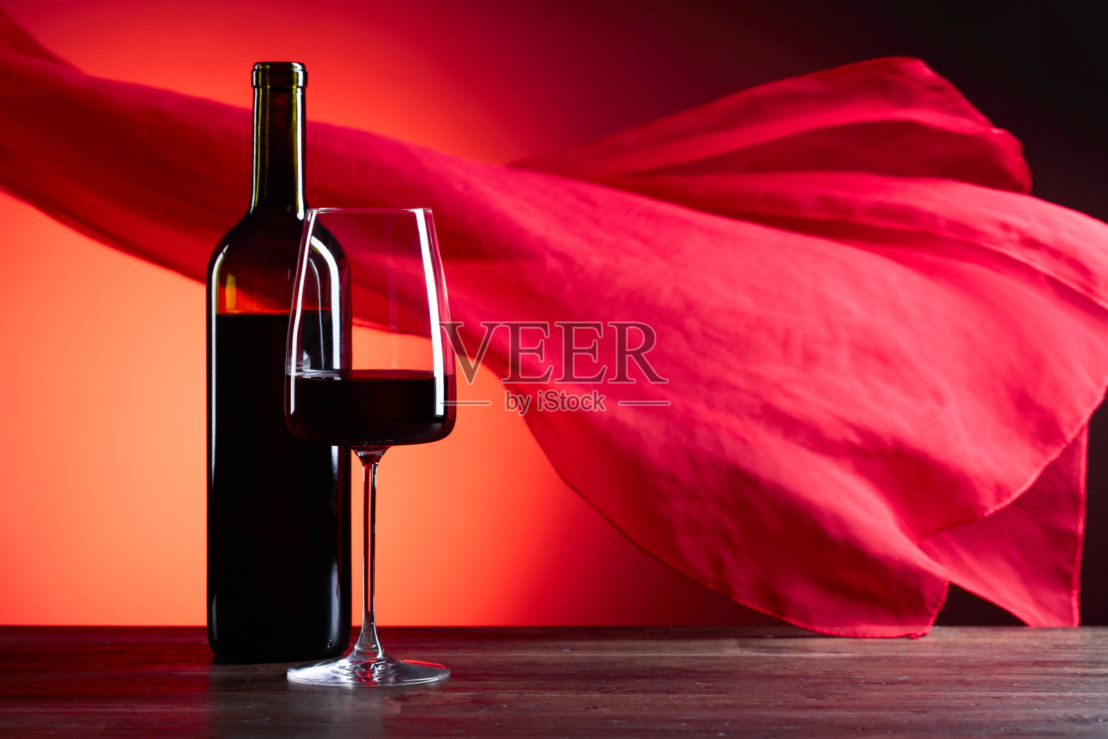 酒杯和酒瓶上的红葡萄酒在红色的背景。红色的薄纱在风中飘动。照片摄影图片