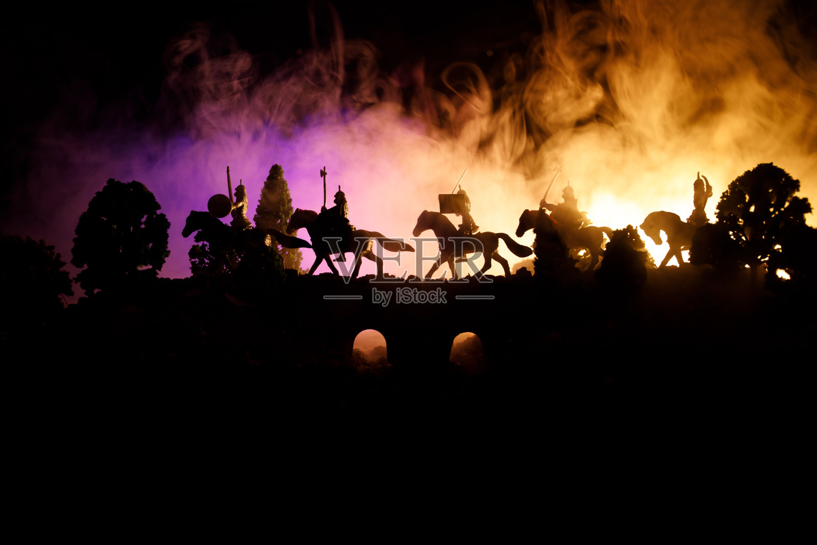 中世纪在桥上与骑兵和步兵的战斗场景。剪影的人物作为单独的对象，战斗的战士之间的黑暗色调的雾背景。夜景。照片摄影图片