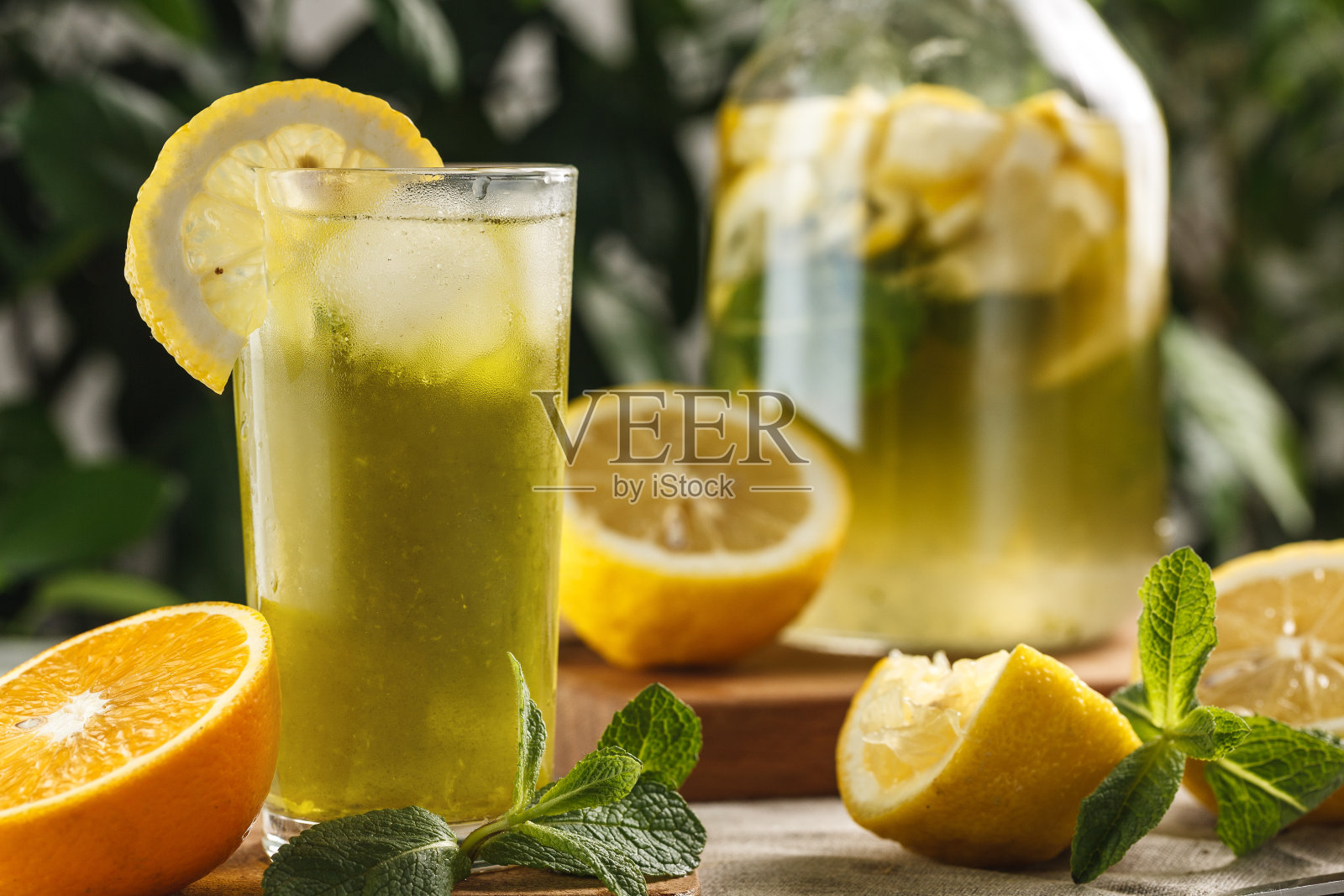 柠檬薄荷柠檬水加冰块，放在玻璃杯里，旁边放着一瓶佳酿。夏天喝Limoncello照片摄影图片