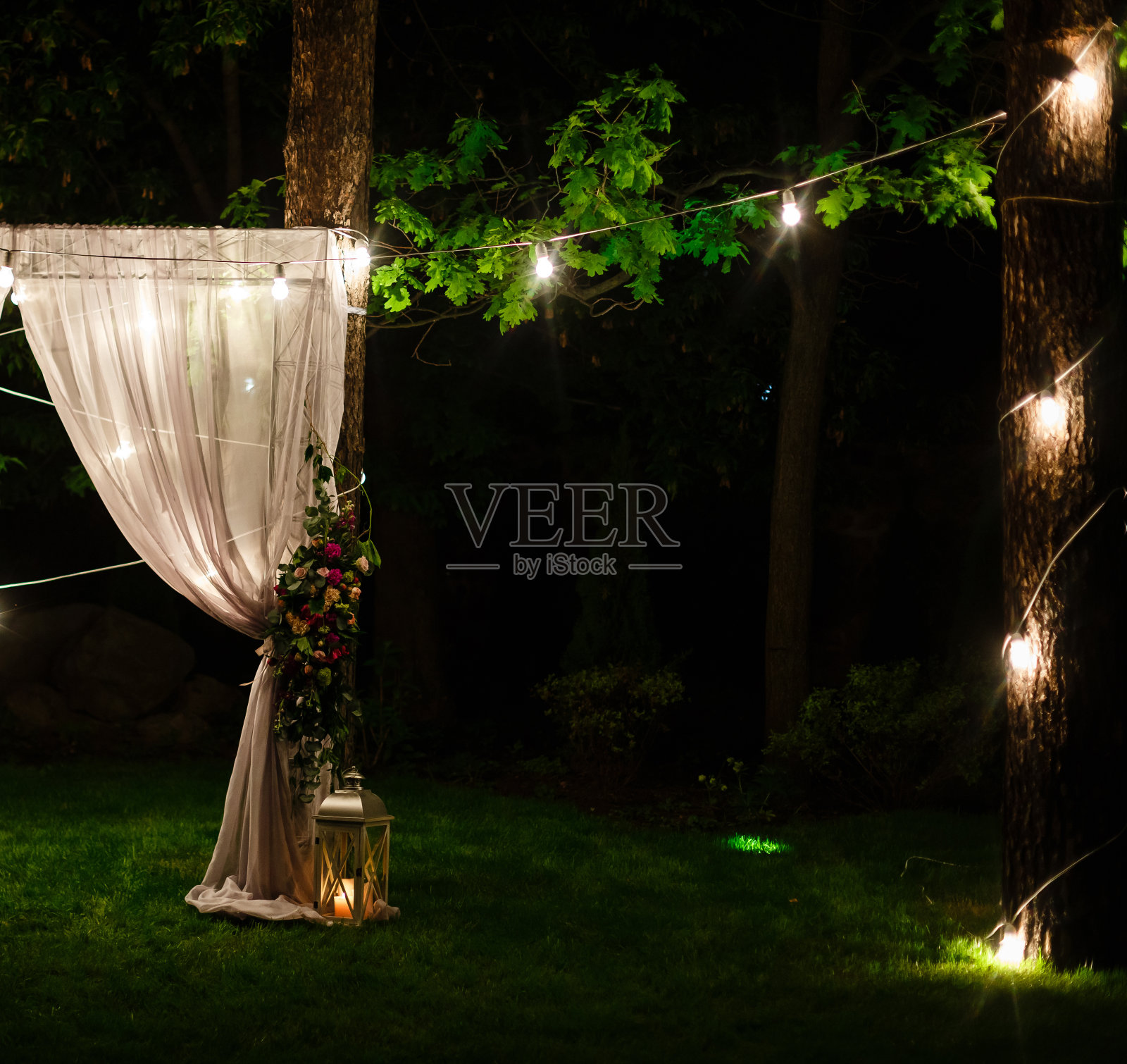 婚礼黄昏仪式上装饰的是挂在树上的金色灯笼和彩灯，站在草地上点燃蜡烛，中间是地毯照片摄影图片