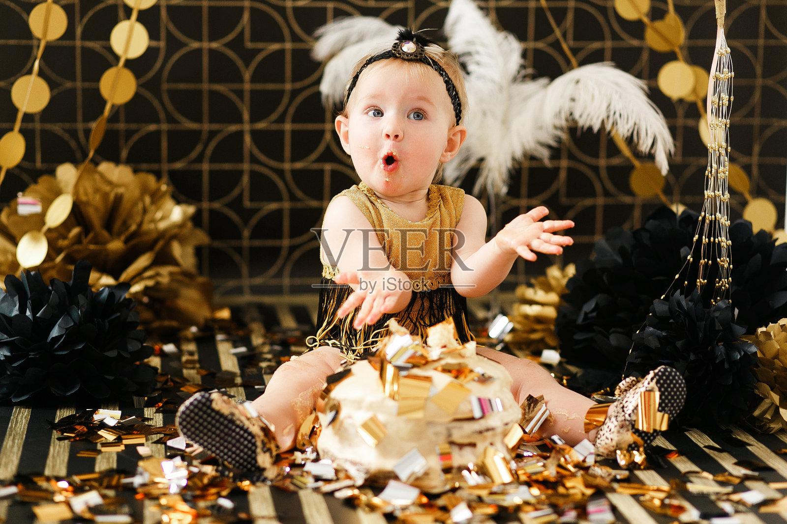 宝宝吃她的第一个生日蛋糕。在黑色和金色的背景下看起来很惊讶照片摄影图片