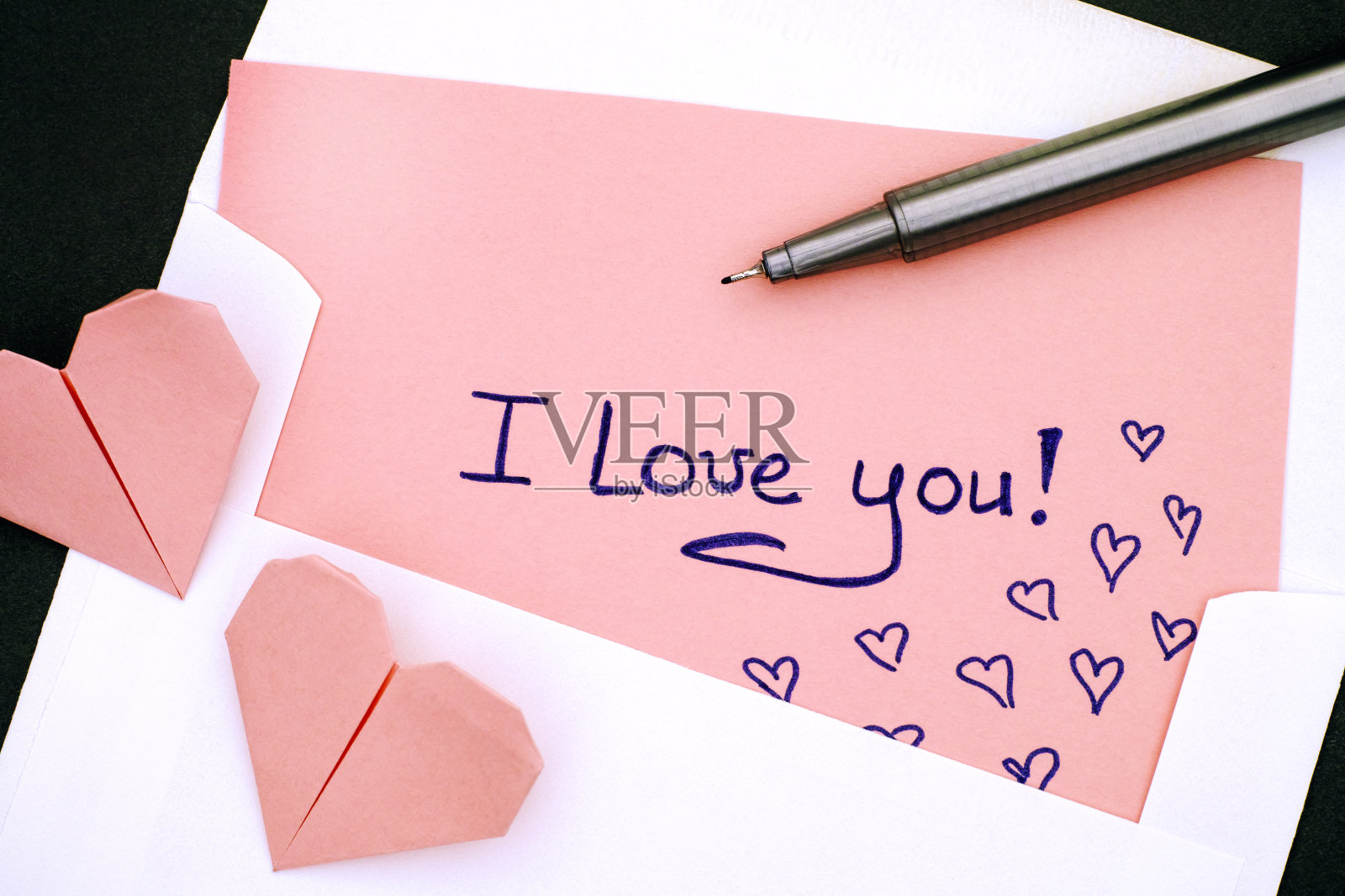 信与文字我爱你!信封里有两颗粉色的折纸心和一支笔。照片摄影图片