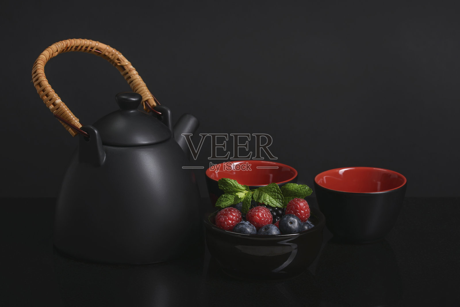 茶具摆放在桌子上，黑色和红色的杯子，上面有黑红色的浆果。照片摄影图片