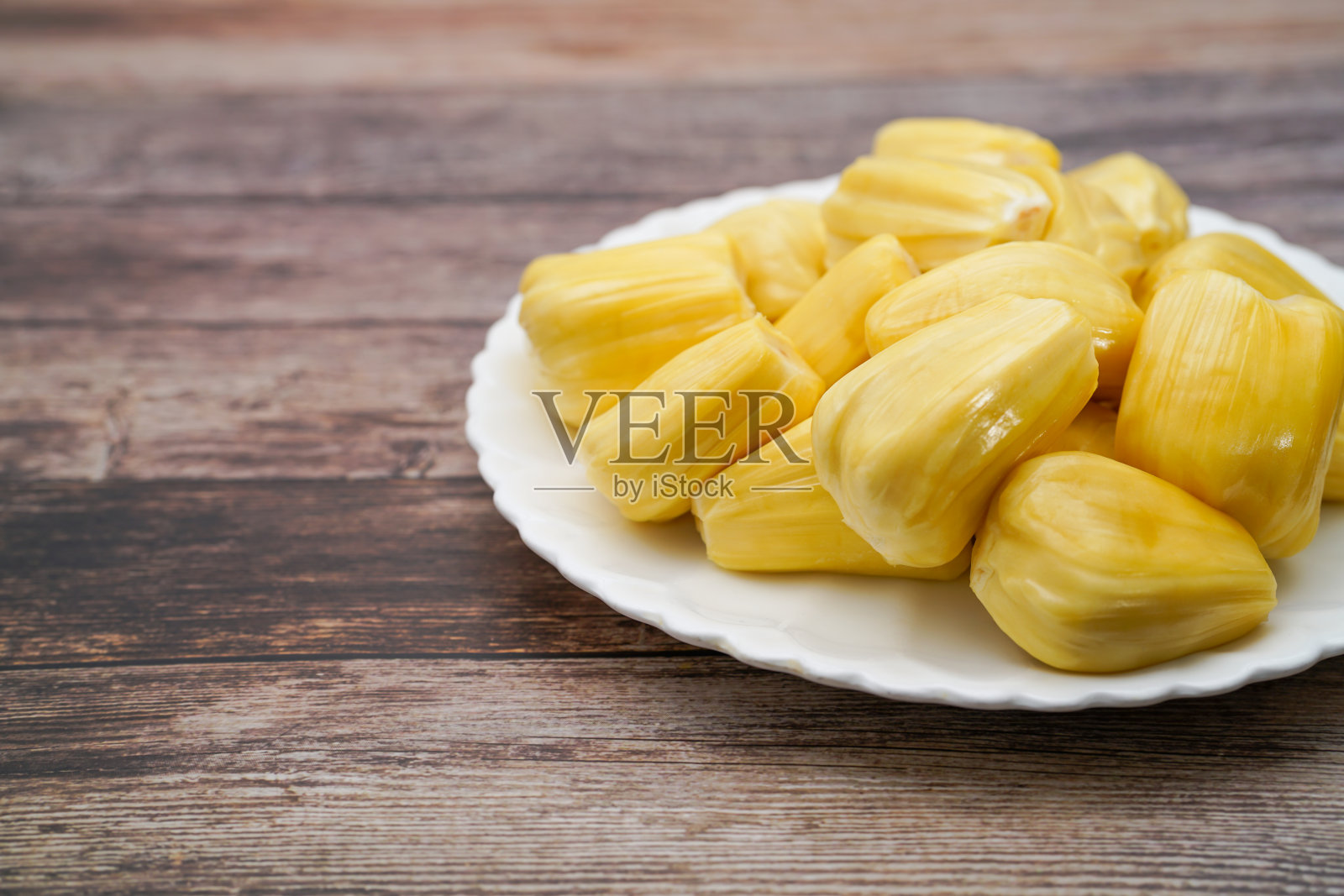 新鲜的菠萝蜜切片放在白色的盘子里。香甜的黄色菠萝蜜成熟了。素食者，纯素食者，生食。奇异的热带水果-孤立照片摄影图片