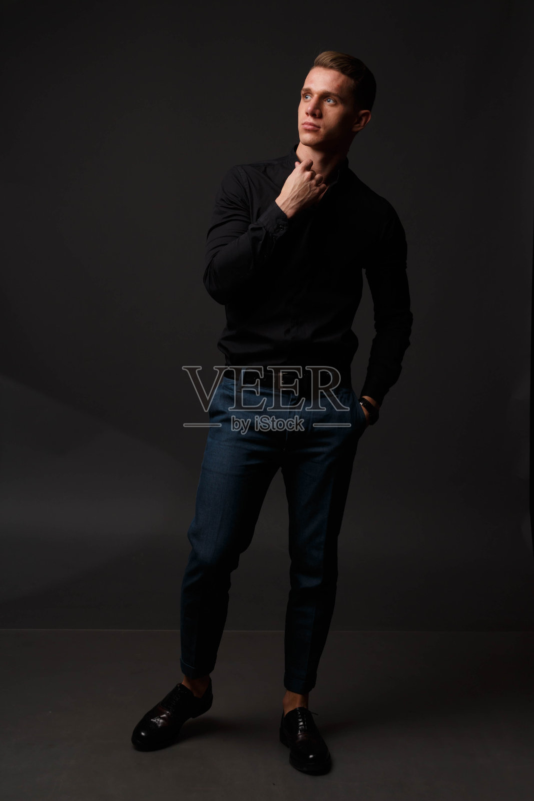 一个穿着黑色衬衫和蓝色裤子的有魅力的白人男子站在黑暗的背景上照片摄影图片