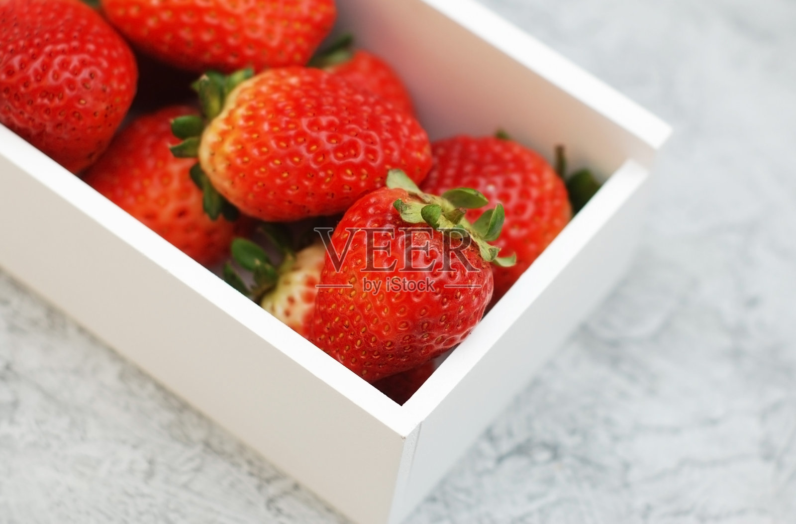 草莓在木制的白色盒子与绿色的叶子收获果实。孤立在白色背景。副本的空间。灰色的背景。照片摄影图片