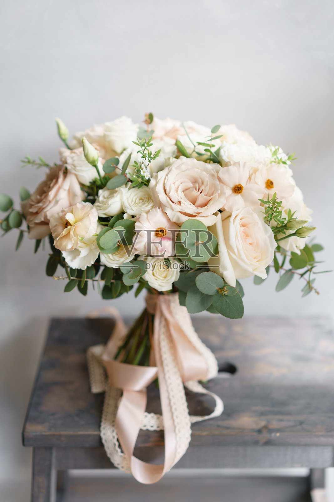木桌上放着一束白玫瑰和毛茛。许多绿色植物，现代的不对称凌乱的新娘束照片摄影图片