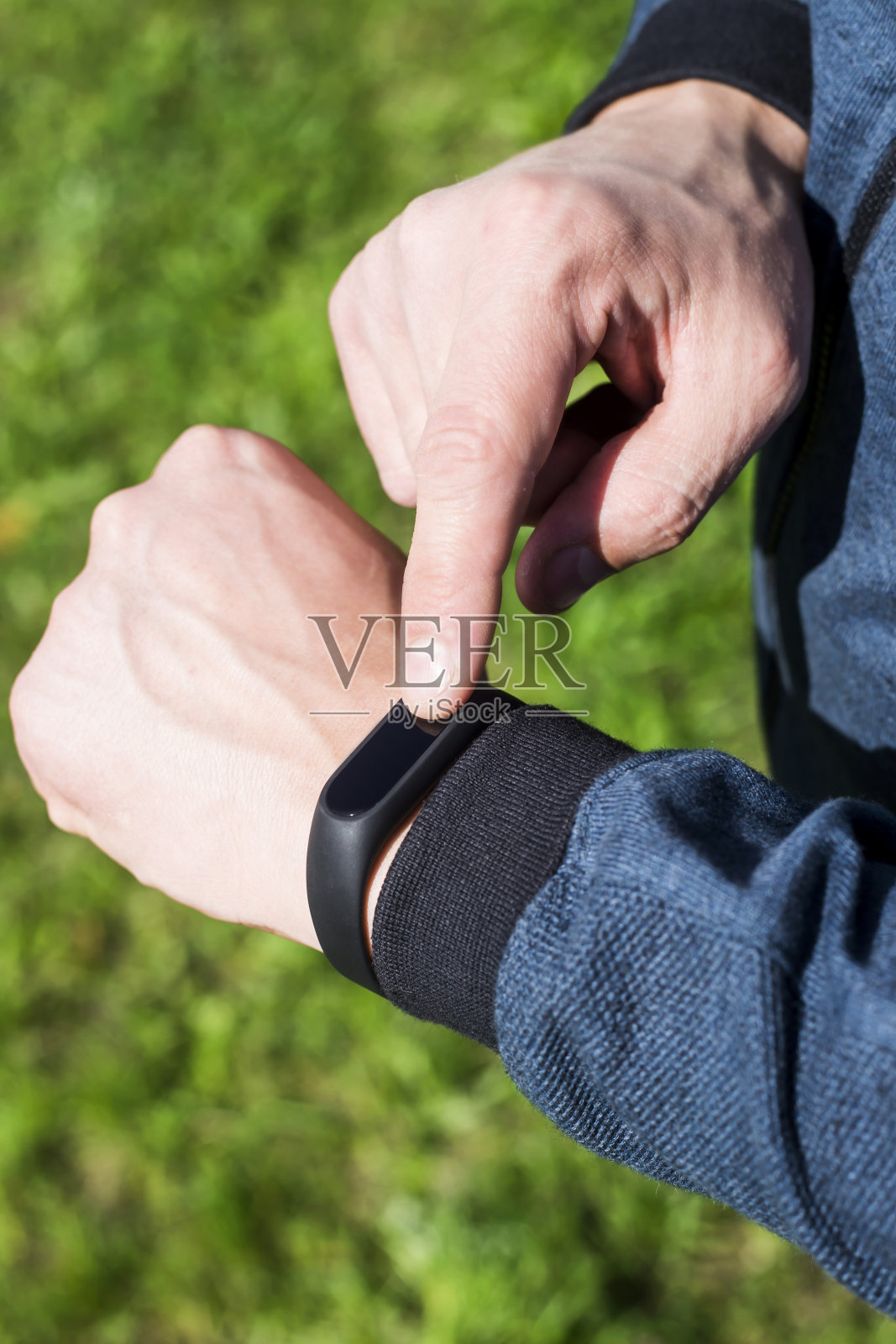 男士手上的健身手镯或智能手表。以绿草为背景。一只带蓝色带子的成年雄性。健康的生活方式的概念照片摄影图片