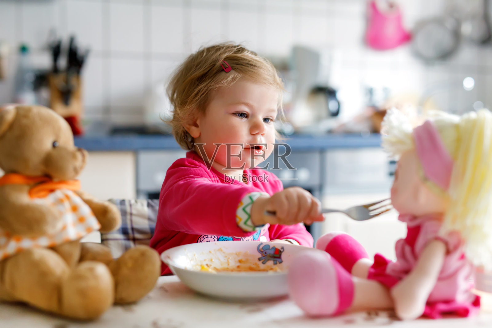 可爱的小女孩用叉子吃蔬菜和意大利面。小孩子吃东西，玩玩具娃娃照片摄影图片