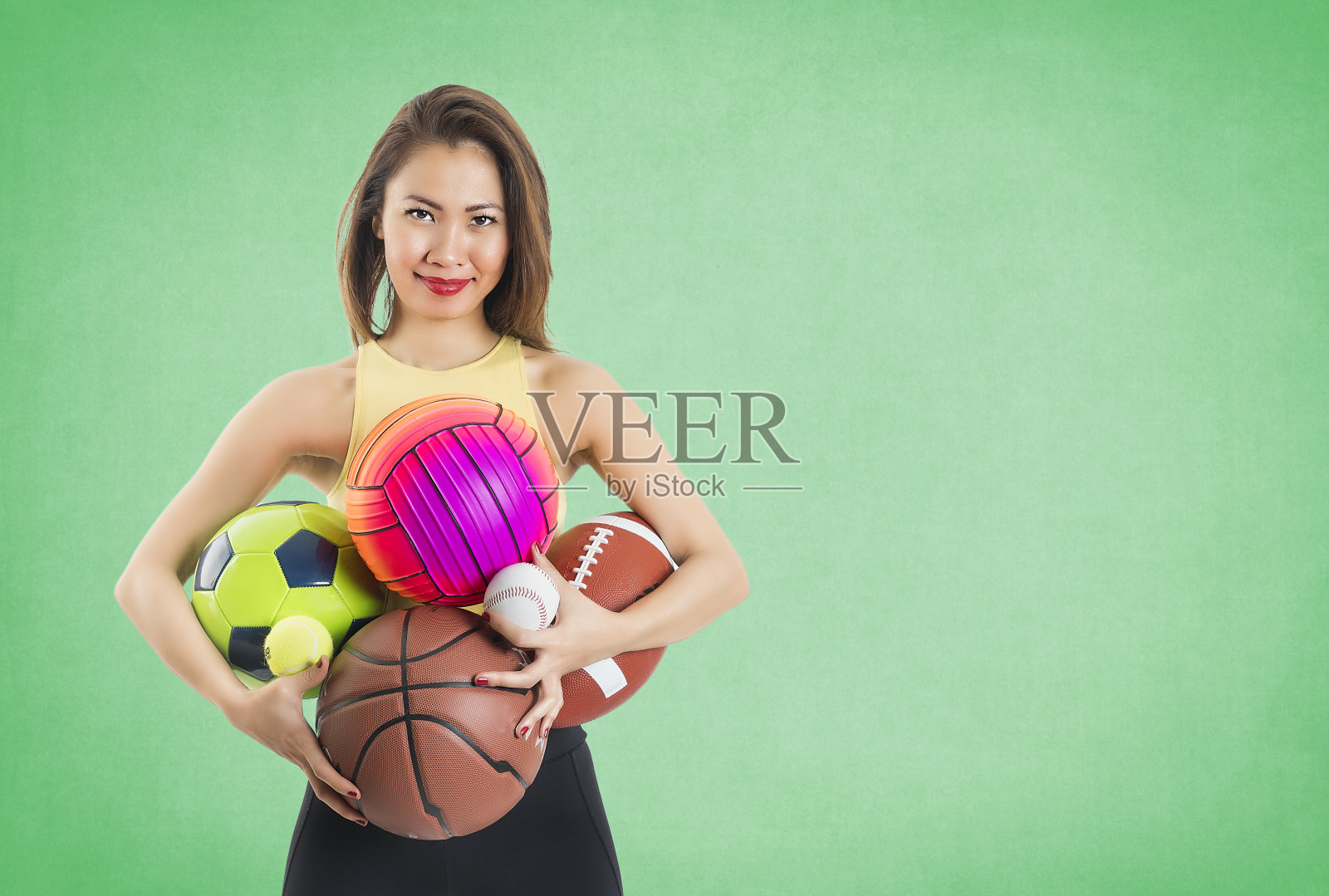 在绿色背景上拿着运动球的亚洲妇女照片摄影图片