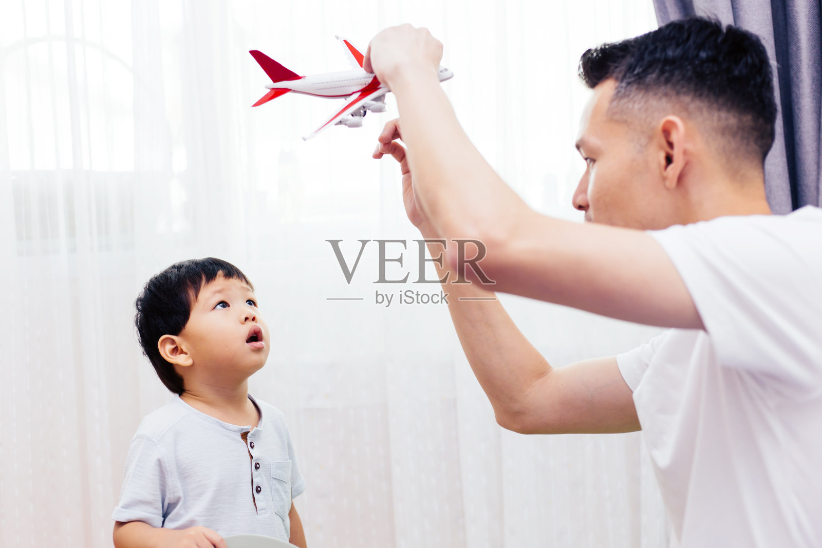 好奇的孩子看着飞机玩具和爸爸一起玩。亚洲家庭在家里一起玩玩具照片摄影图片