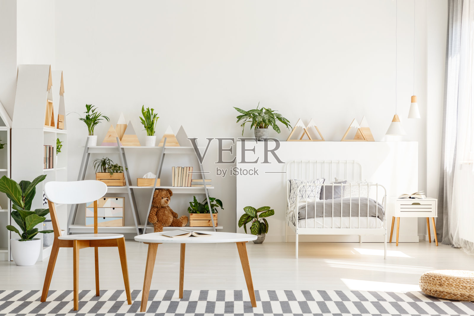 木制的椅子和桌子与打开的书放在地毯上，明亮的斯堪的纳维亚风格的卧室室内的真实照片与金属床，新鲜的植物和三角架照片摄影图片