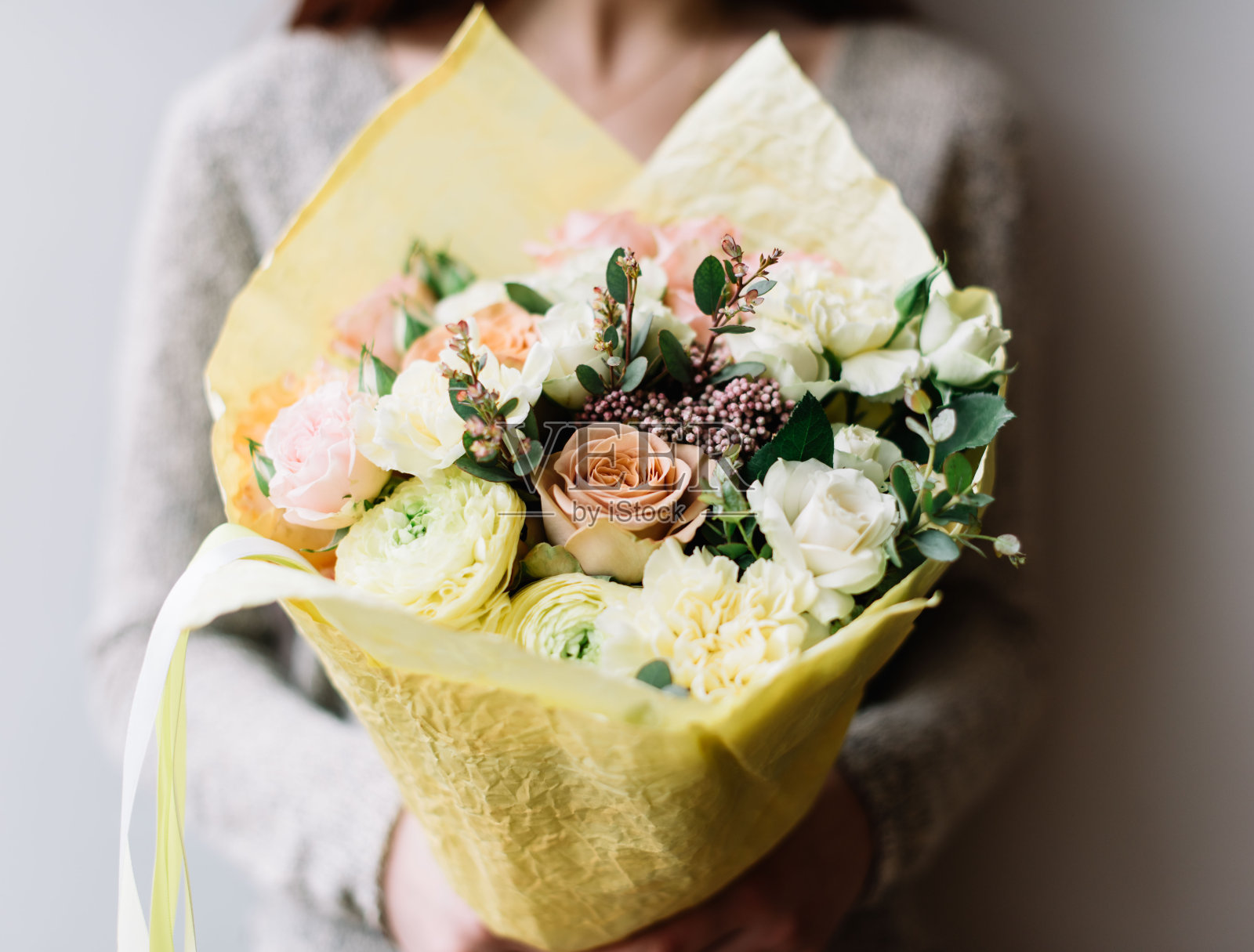 非常漂亮的年轻女子捧着一朵朵新鲜的毛茛、玫瑰、康乃馨、桉树花束，在灰色的墙壁背景上，有淡粉色和柠檬黄的颜色照片摄影图片