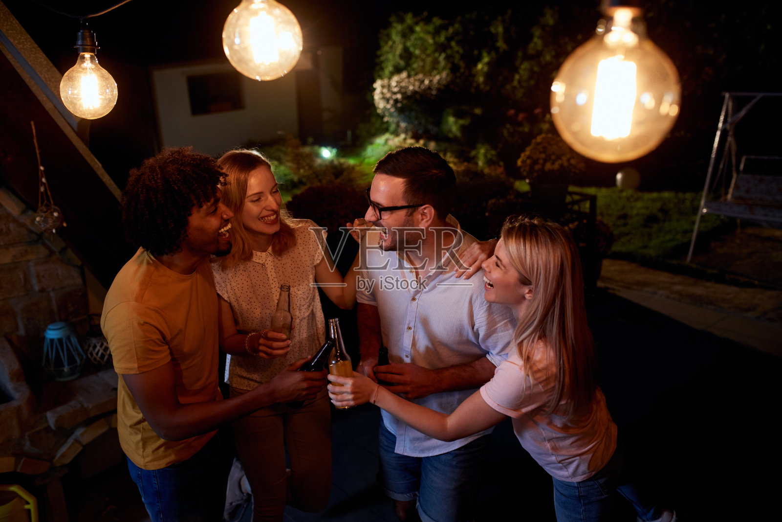 愉快的朋友们晚上在露台上举行饮酒聚会。照片摄影图片