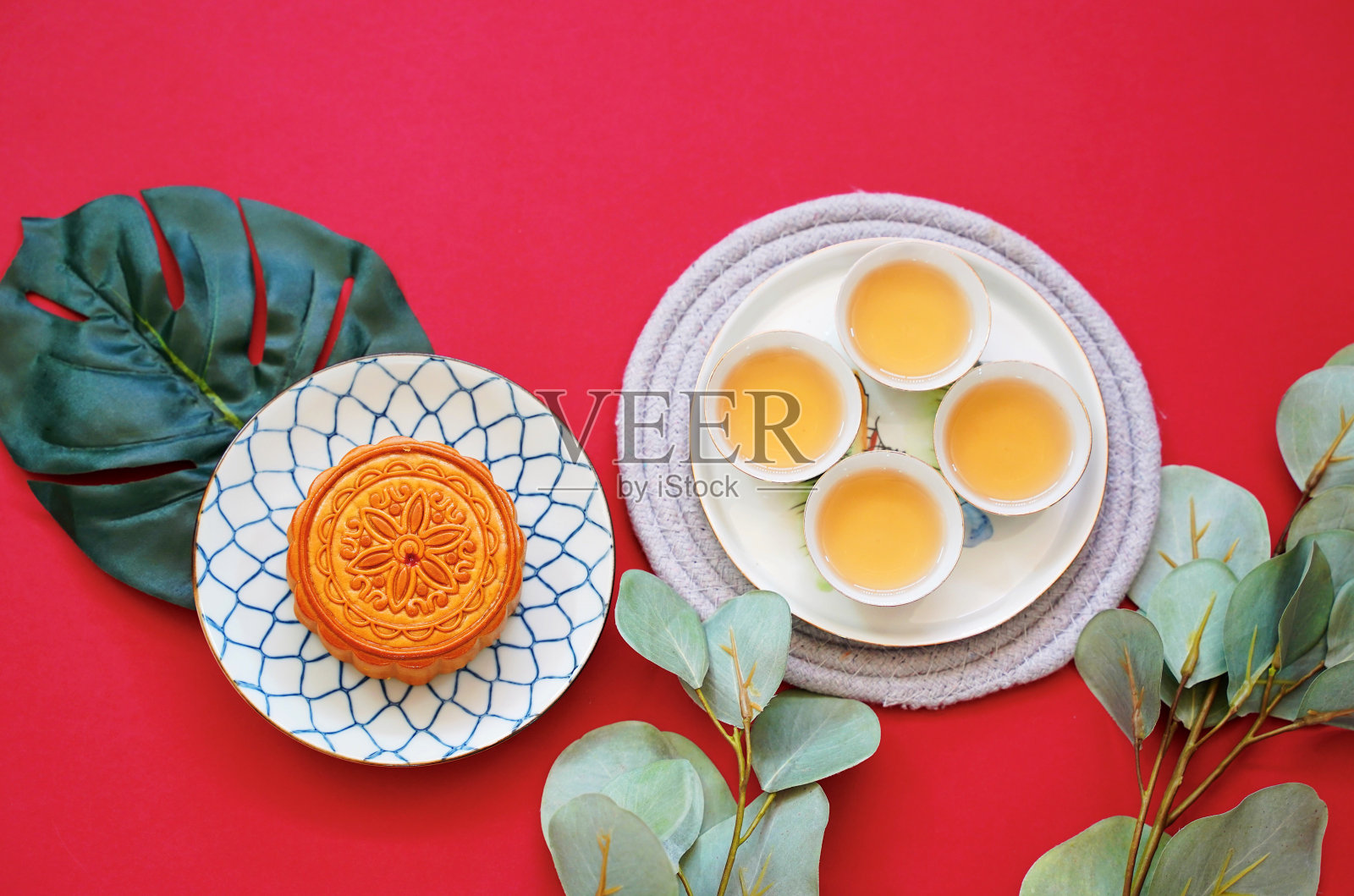 平铺的中国月饼与热茶和绿色植物在红色的背景，节日和节日的概念照片摄影图片