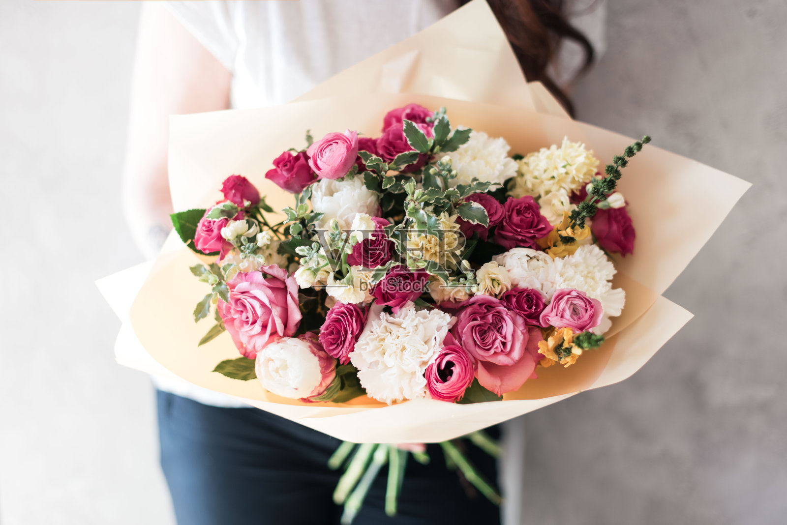 非常漂亮的年轻女子捧着一朵朵新鲜的玫瑰，毛茛，桔梗，桉树在灰色的墙壁背景上的粉红色的花束照片摄影图片