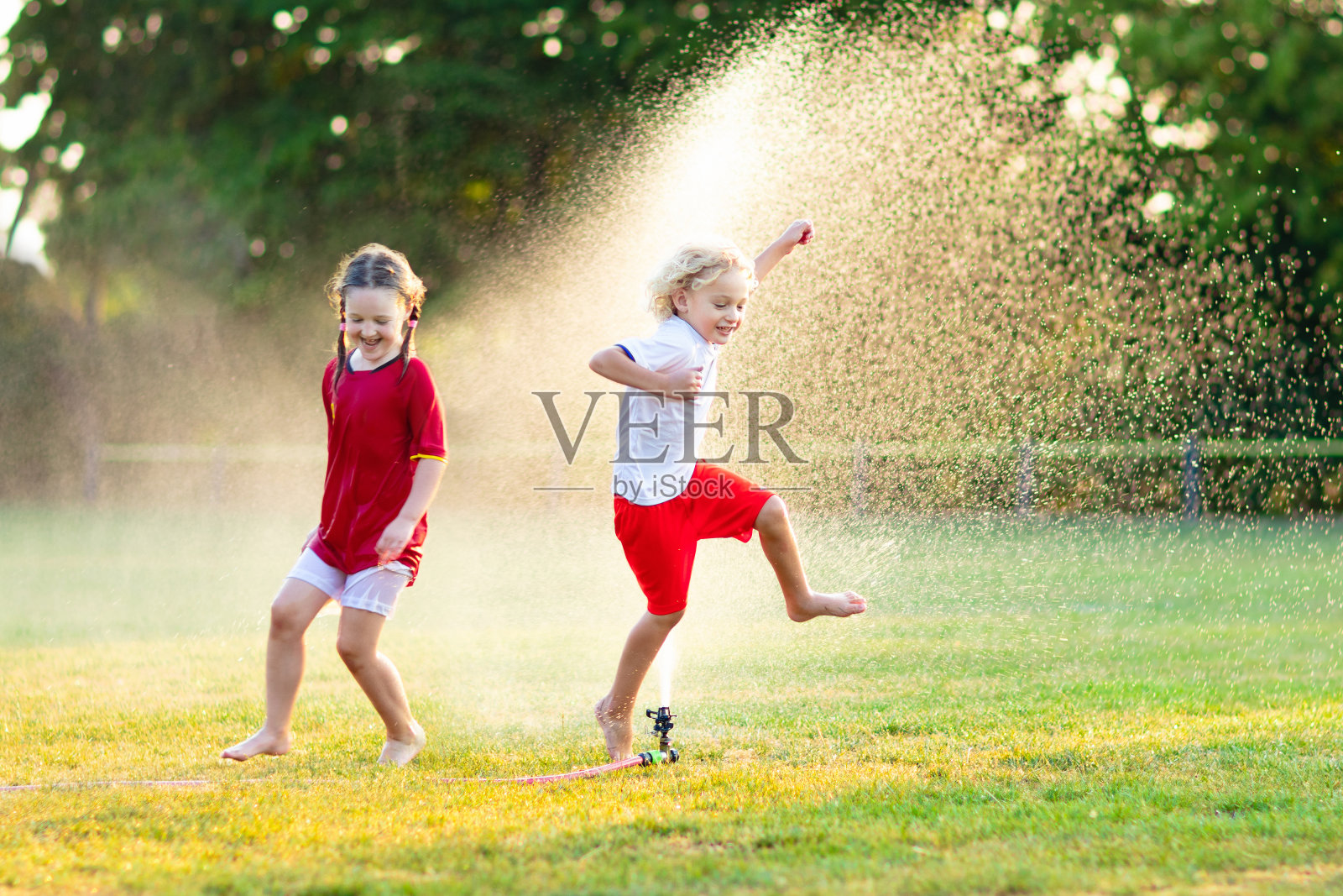 孩子们玩水。孩子与花园洒水喷头。照片摄影图片