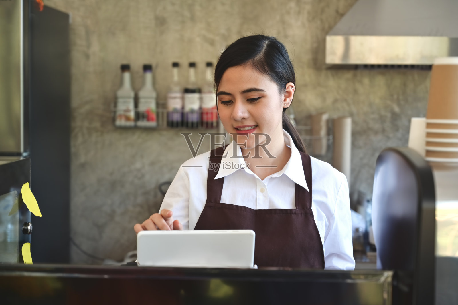 亚洲女性咖啡师微笑着使用平板电脑在咖啡店柜台点菜照片摄影图片