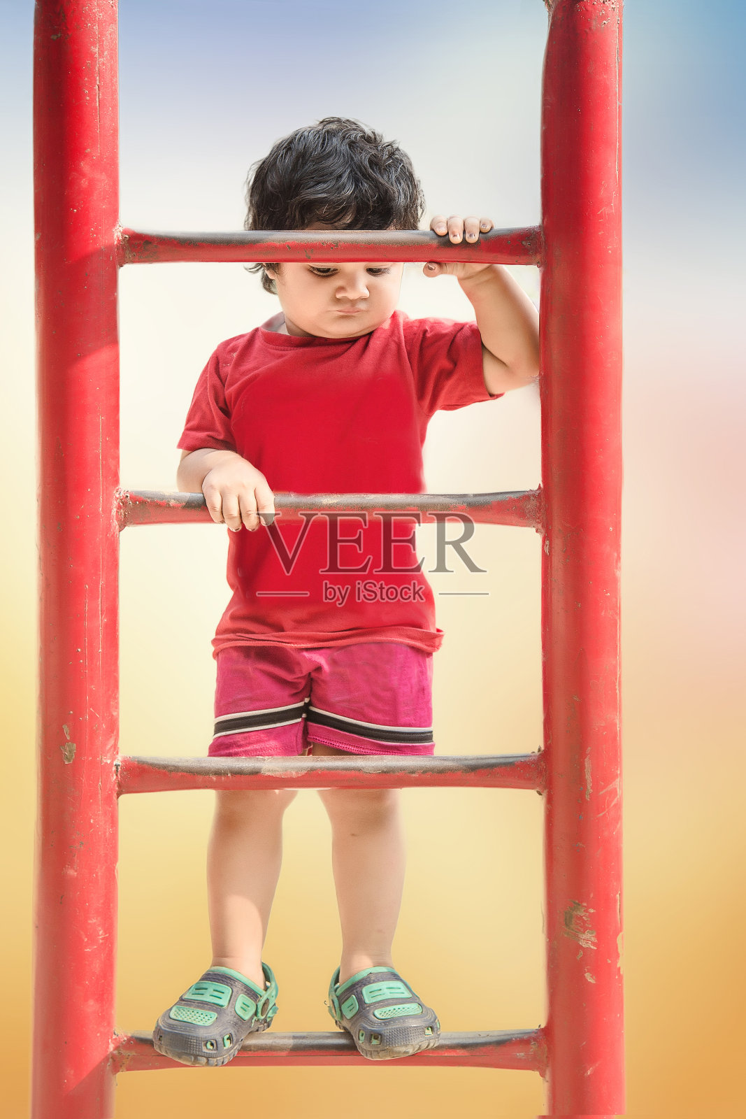 悲哀孤独可爱可爱的印度小婴儿的肖像，在操场上爬上铁梯。照片摄影图片