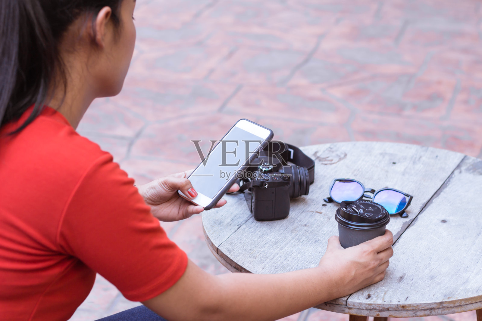 小女孩正在用手机玩网络，木桌上放着照相机、太阳镜、咖啡杯。照片摄影图片