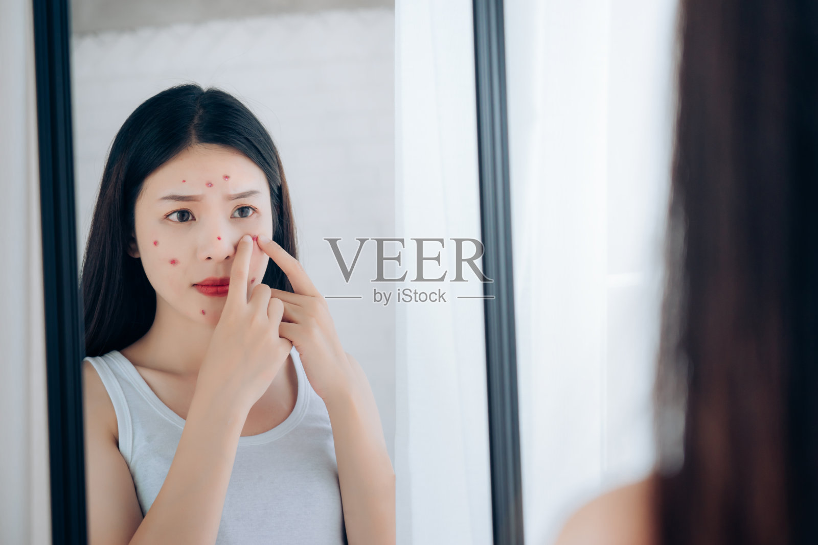 年轻的亚洲女人在照镜子时脸上挤痘痘问题她没有护肤。照片摄影图片