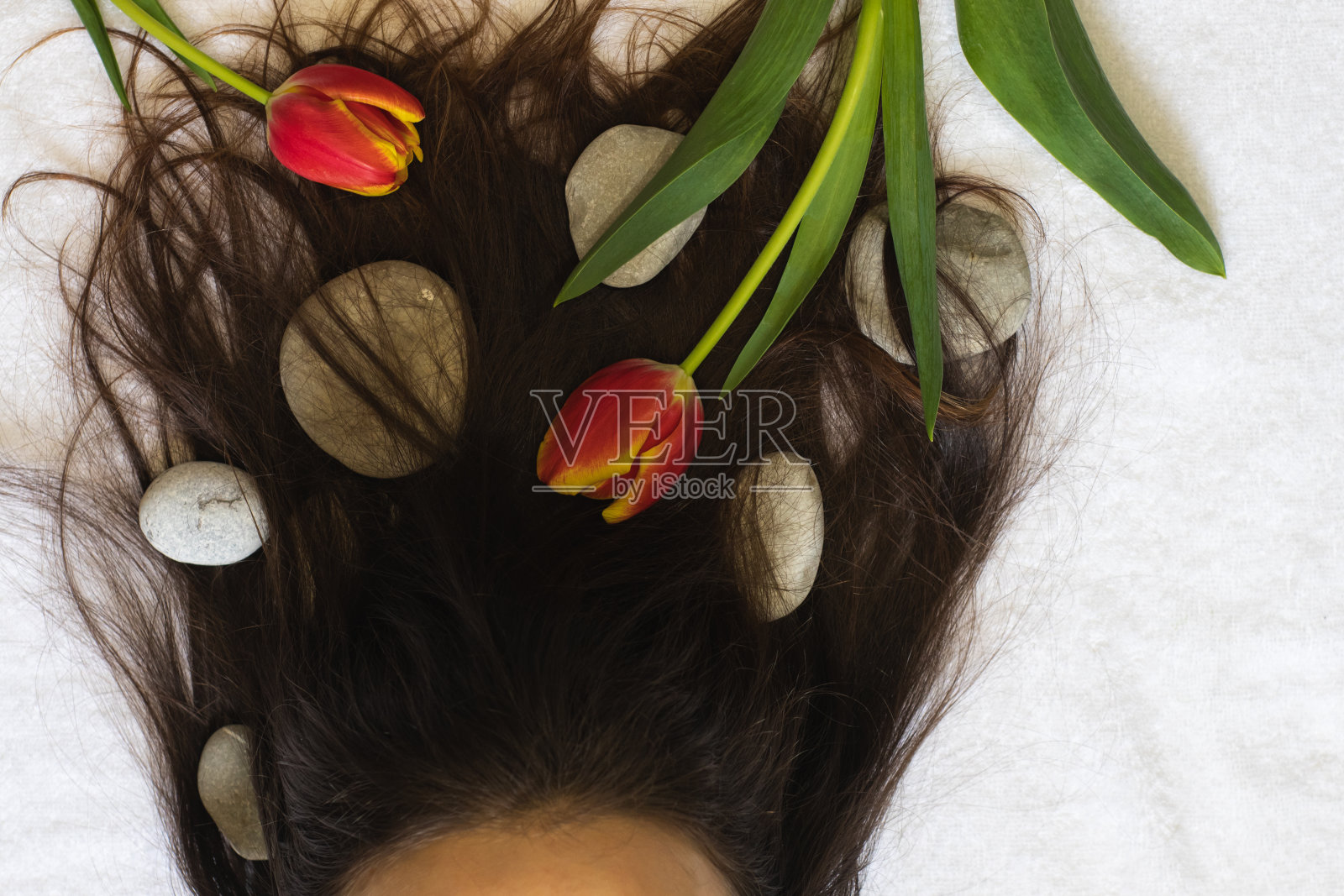 年轻女孩的头发被温泉石和郁金香缠绕着照片摄影图片