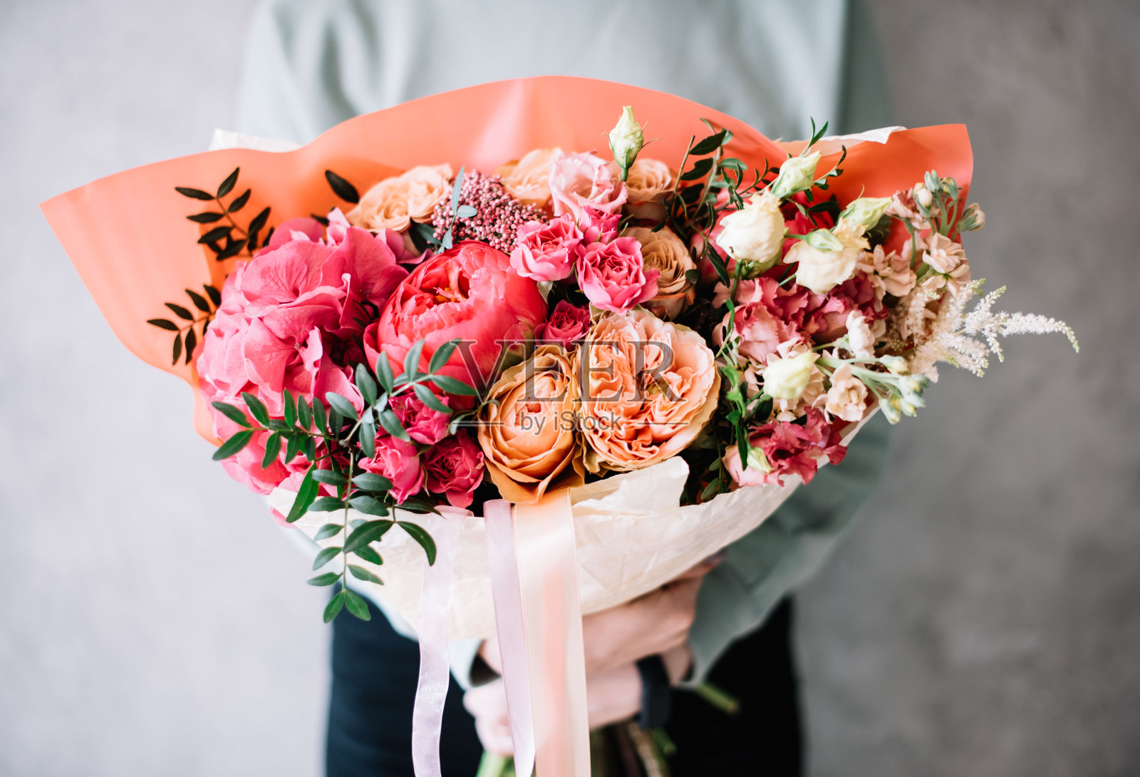 非常漂亮的年轻女子手持一束美丽的鲜花，新鲜的牡丹，玫瑰，菊芋，开心果，康乃馨在嫩粉色和鲜艳的洋红颜色的灰色背景照片摄影图片