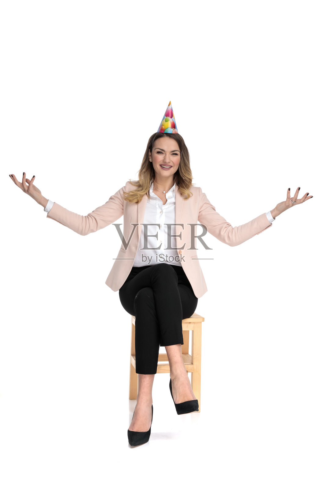 坐时髦随意的女人戴着生日帽做问候手势照片摄影图片
