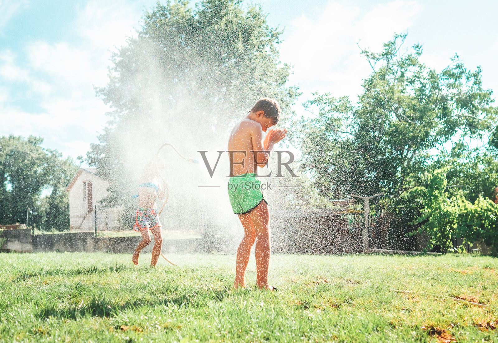炎炎夏日的活动:快乐的小女孩跳入水中，当哥哥把她从花园里的软管里倒出来时照片摄影图片
