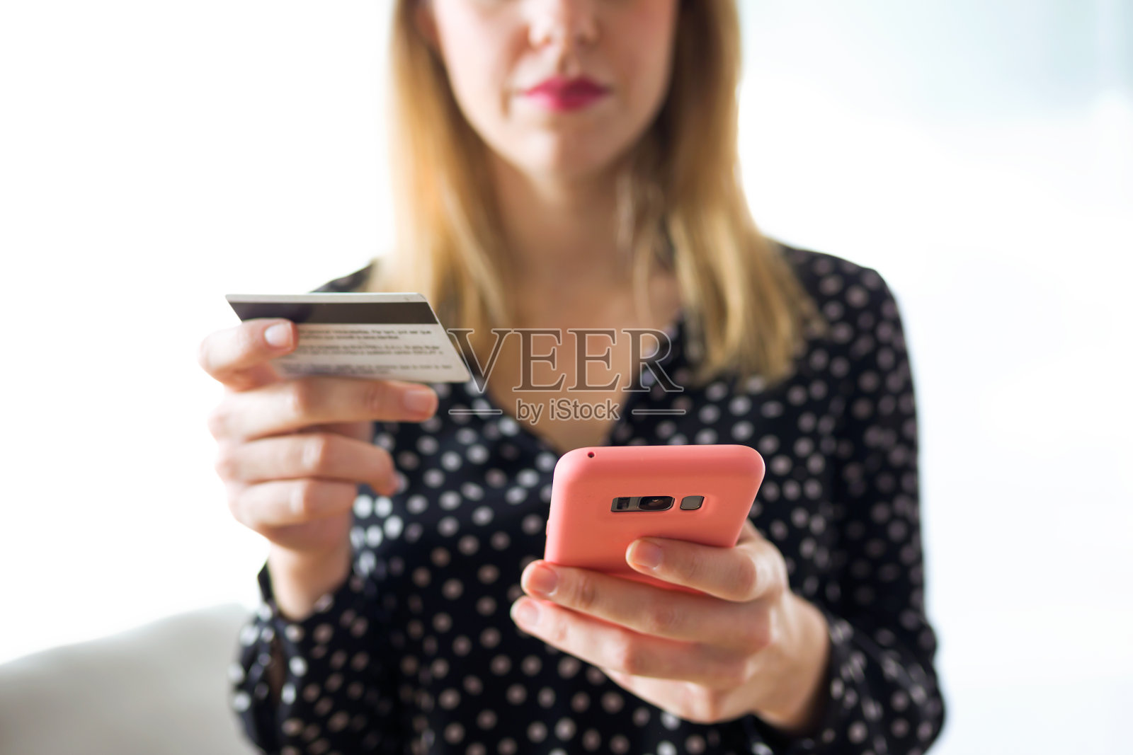 拿着白色信用卡，在家里客厅用手机网购的严肃年轻女子。照片摄影图片