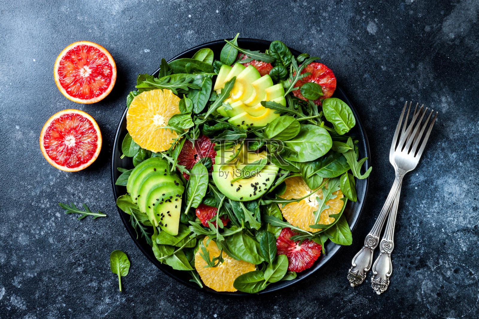 黑色陶瓷盘子上放着柑橘沙拉，混合绿叶蔬菜和血橙。纯素、素食、清洁饮食、节食、饮食观念。黑石的背景。照片摄影图片