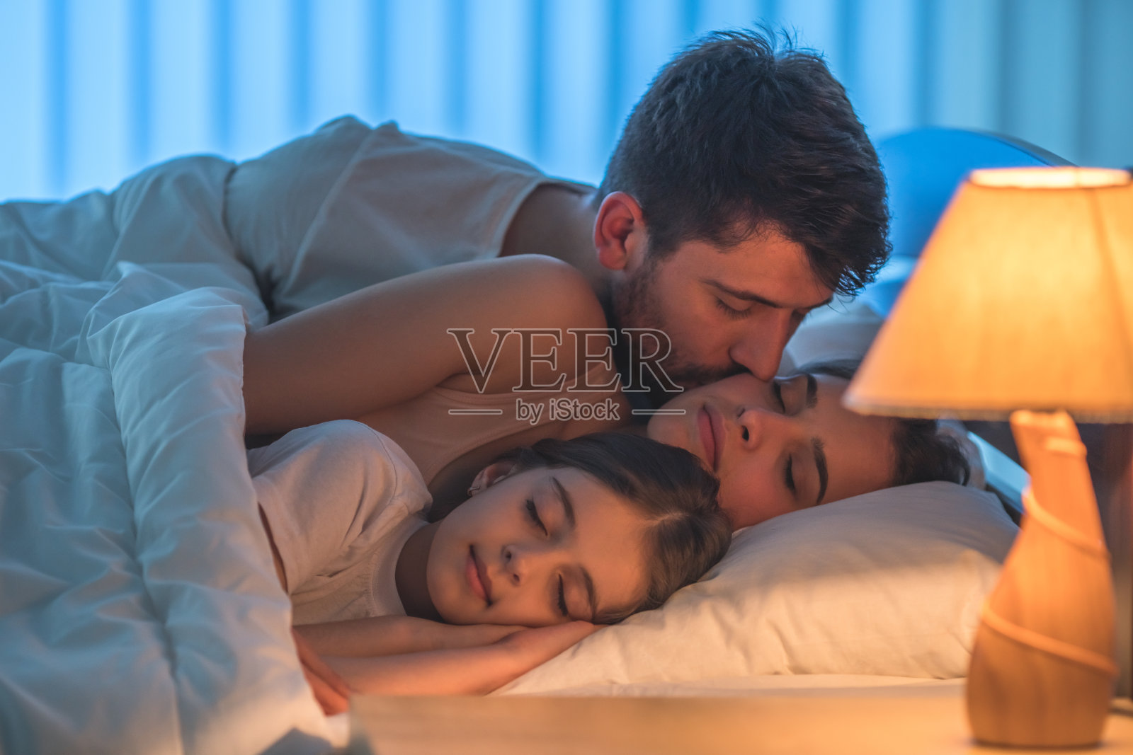 在床上的女儿旁边，男人亲吻着一个女人。晚上的时间照片摄影图片