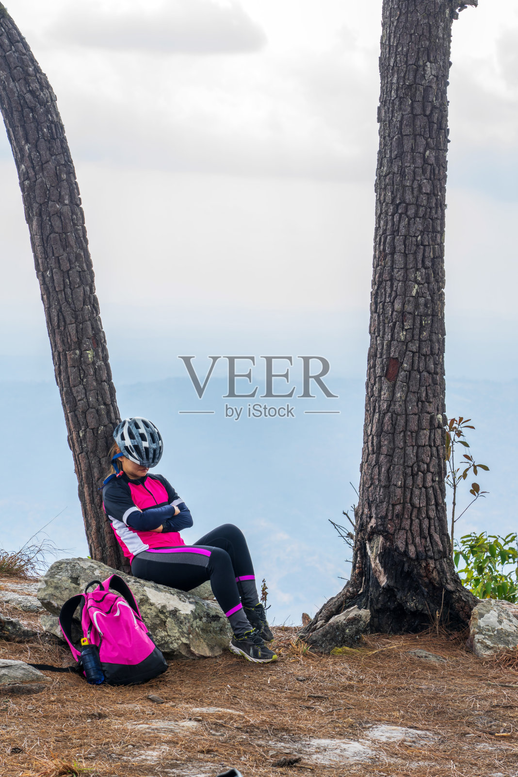 亚洲女自行车运动员睡在岩石悬崖上靠在树上照片摄影图片