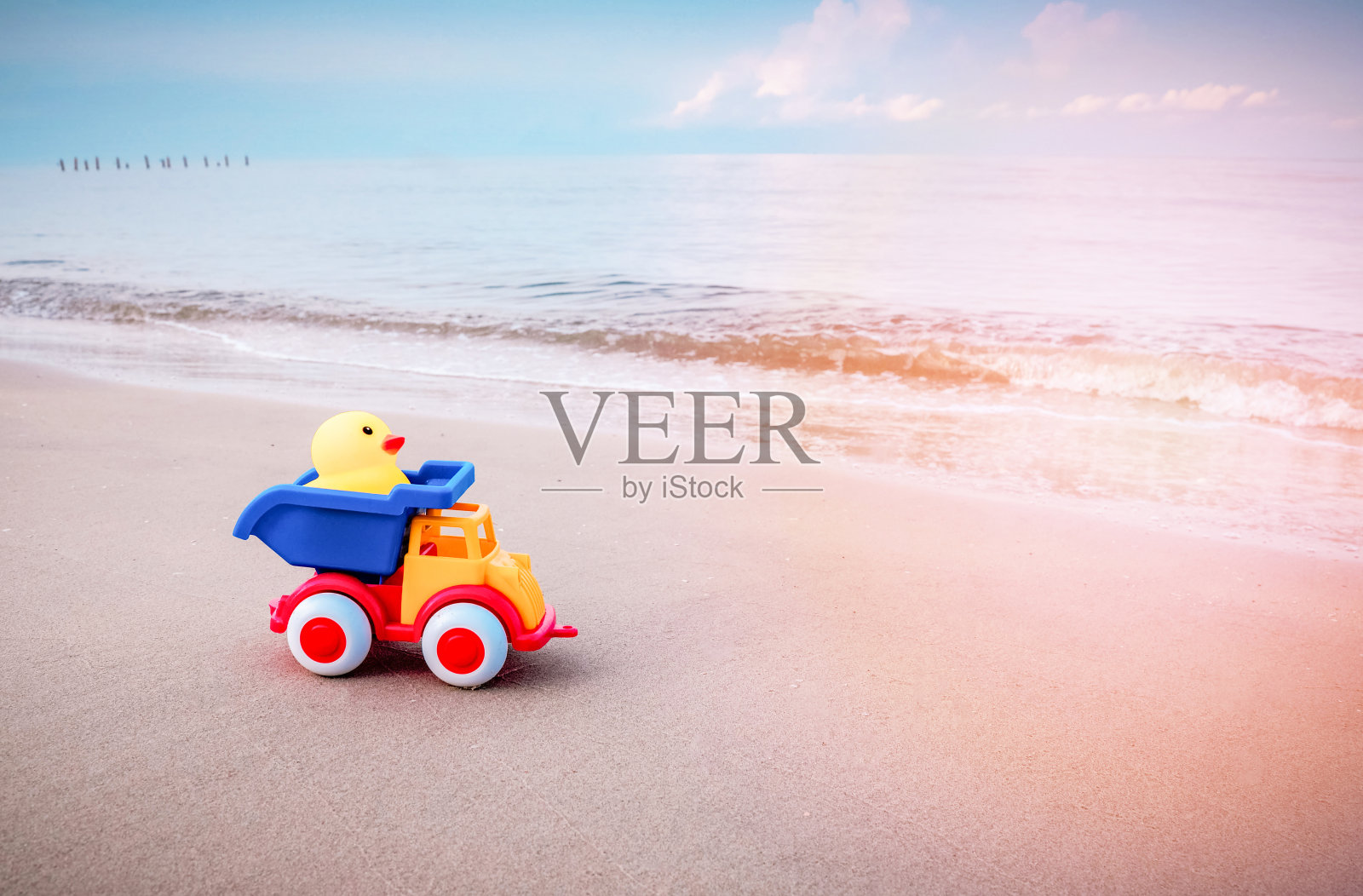 黄色的鸭子玩具和五颜六色的汽车在沙滩上照片摄影图片
