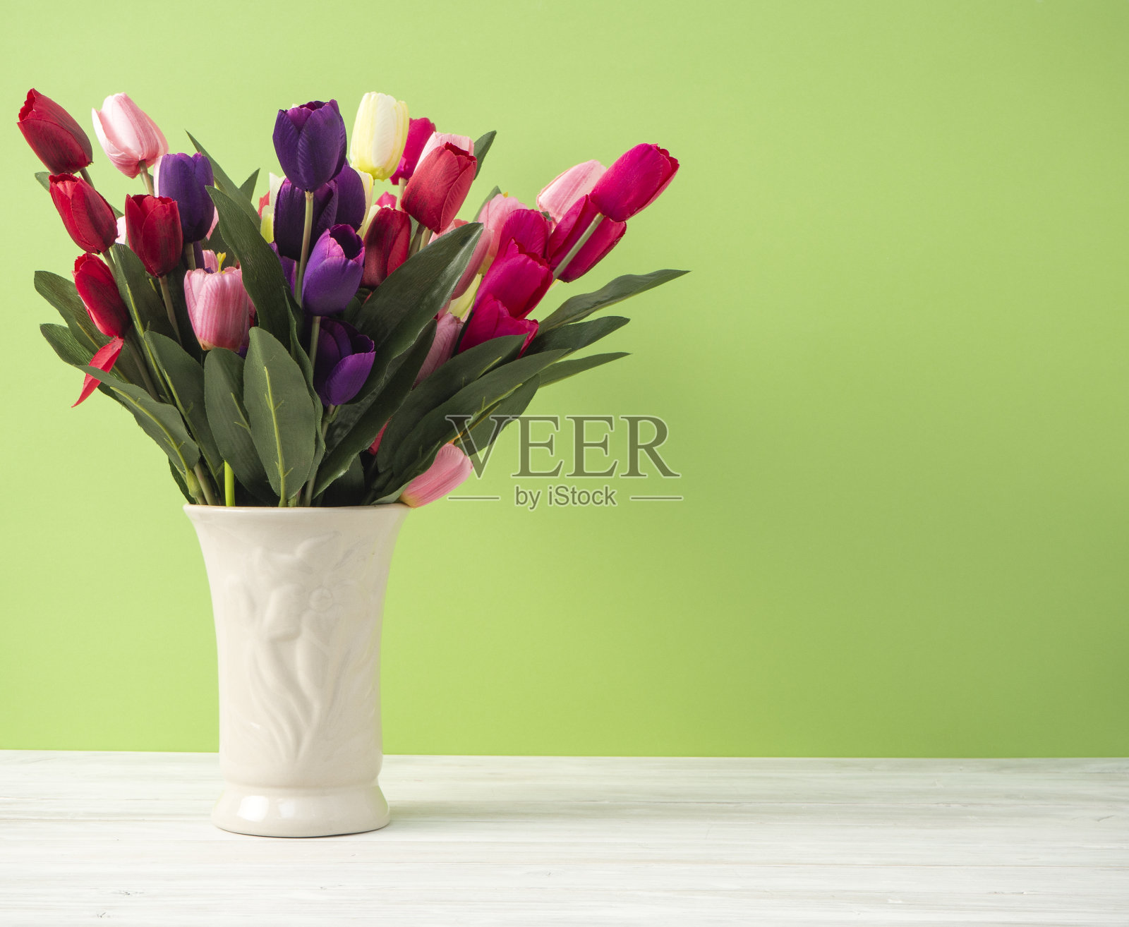淡绿色背景的桌上，白色花瓶里插着五颜六色的郁金香照片摄影图片