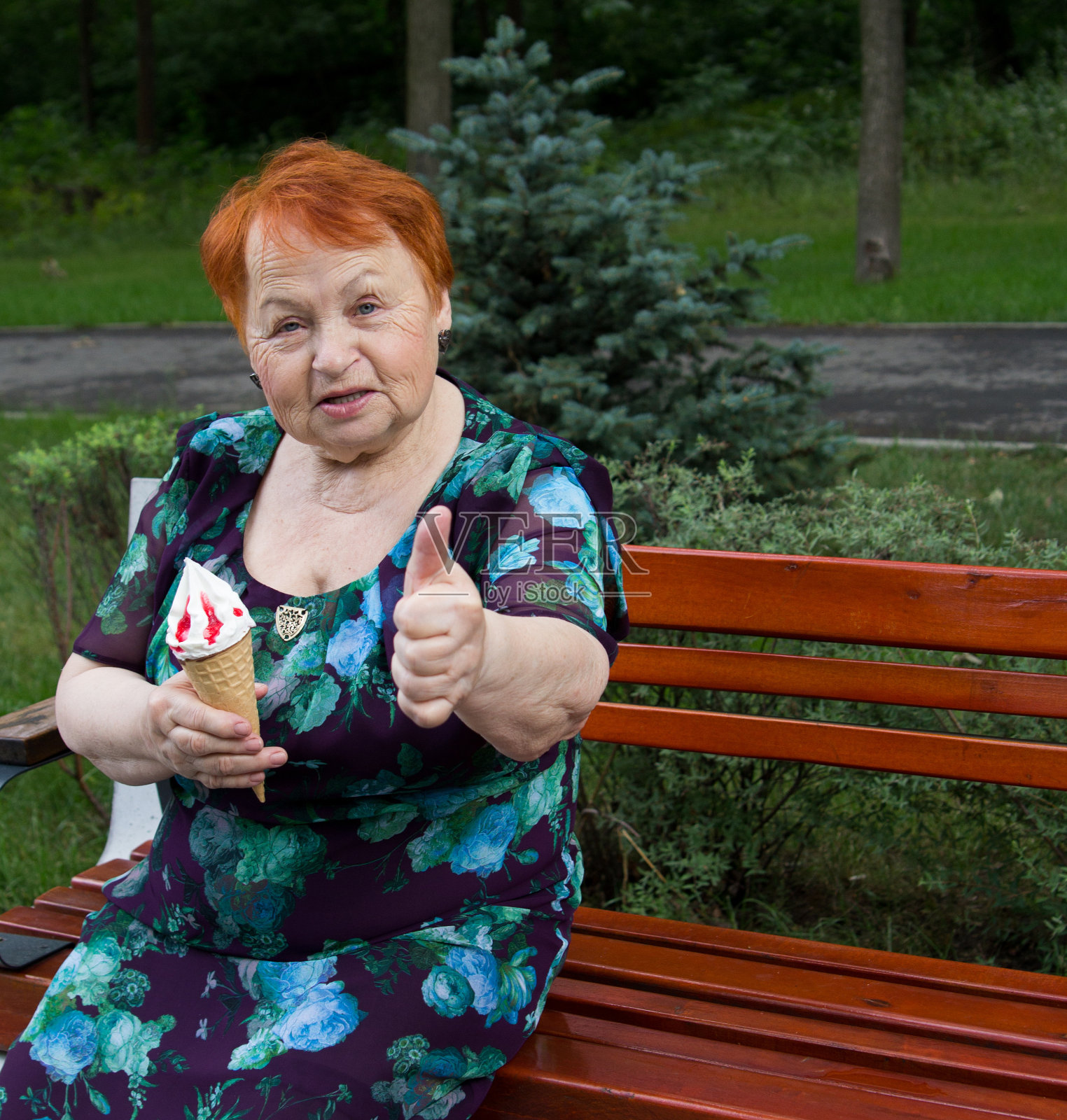 快乐的老妇人吃着冰淇淋，夏天老妇人坐在公园的长凳上吃着冰淇淋照片摄影图片