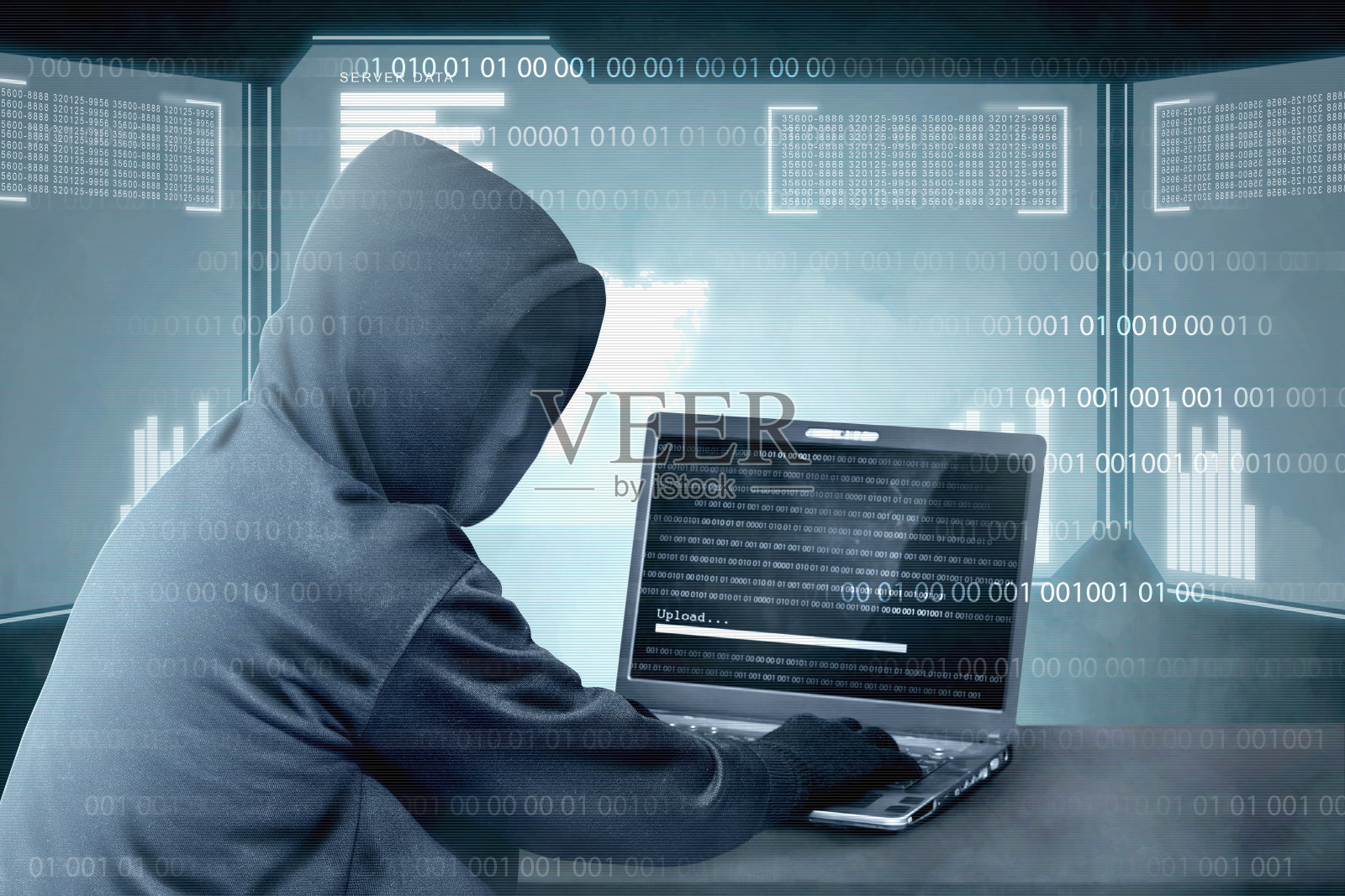 穿着黑帽衫的黑客用桌上的笔记本电脑用二进制代码入侵系统并上传恶意软件照片摄影图片