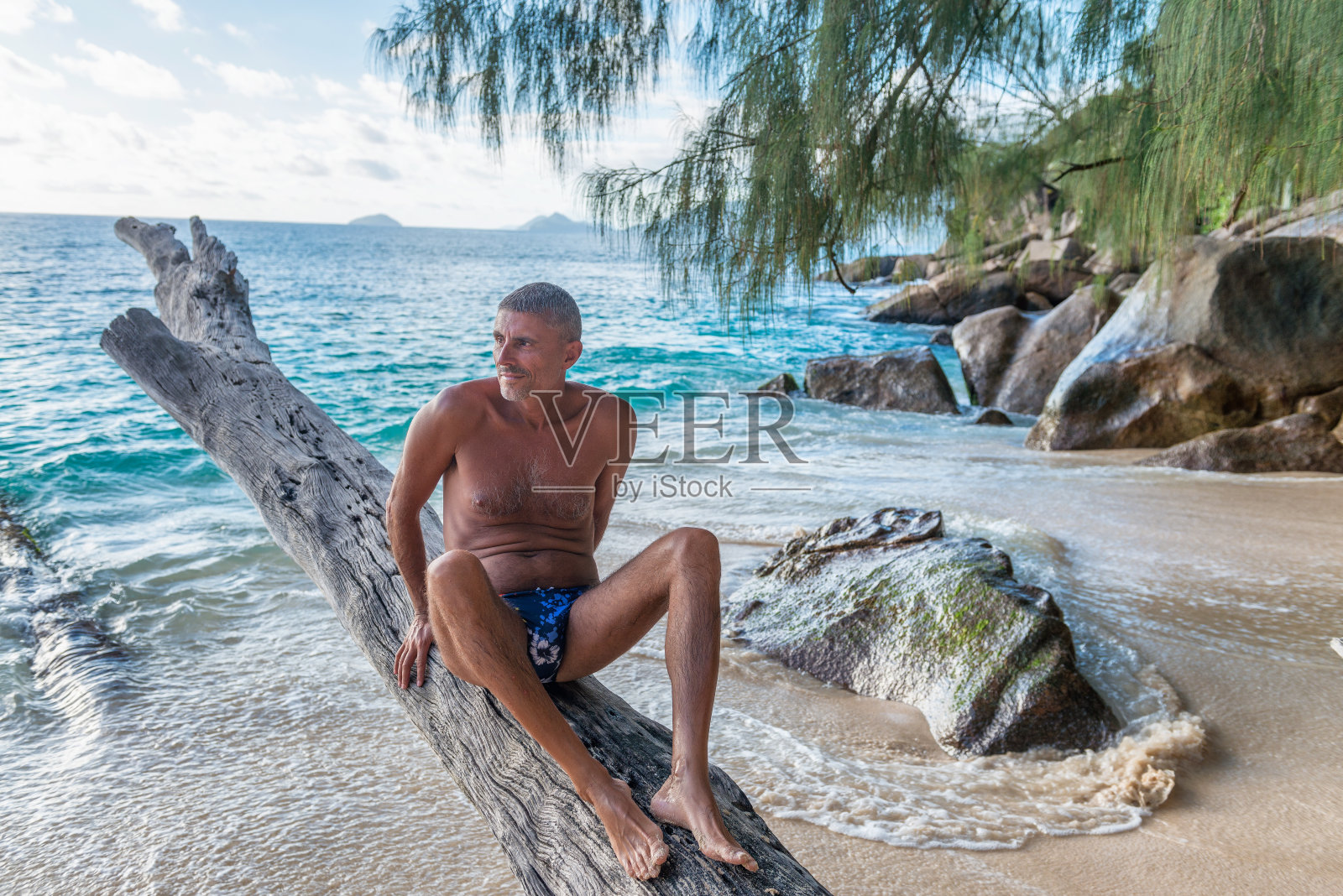 四十多岁的男人坐在树干上。热带度假概念照片摄影图片
