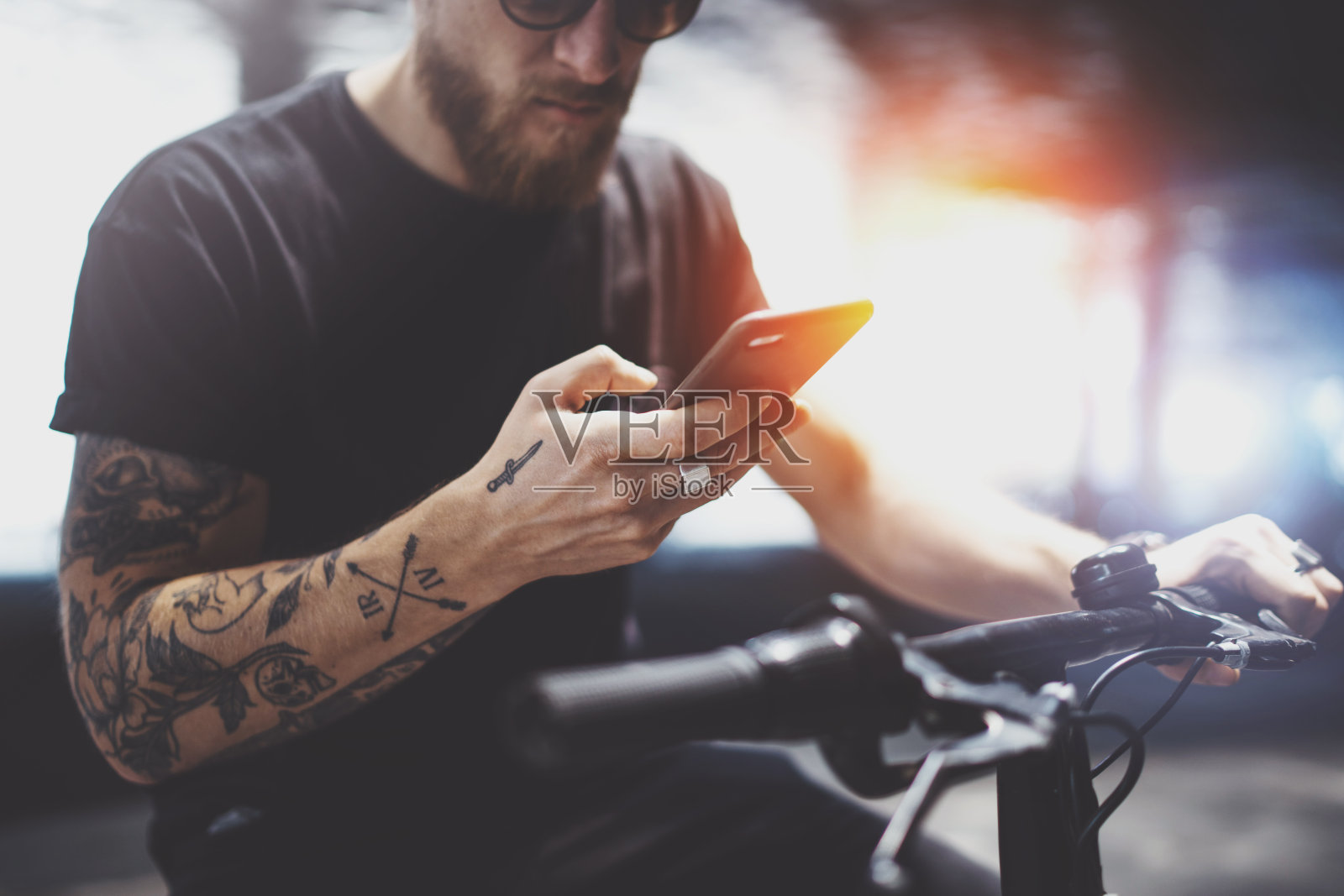 一名戴着墨镜的纹身男子骑着电动车在城市里发短信。照片摄影图片