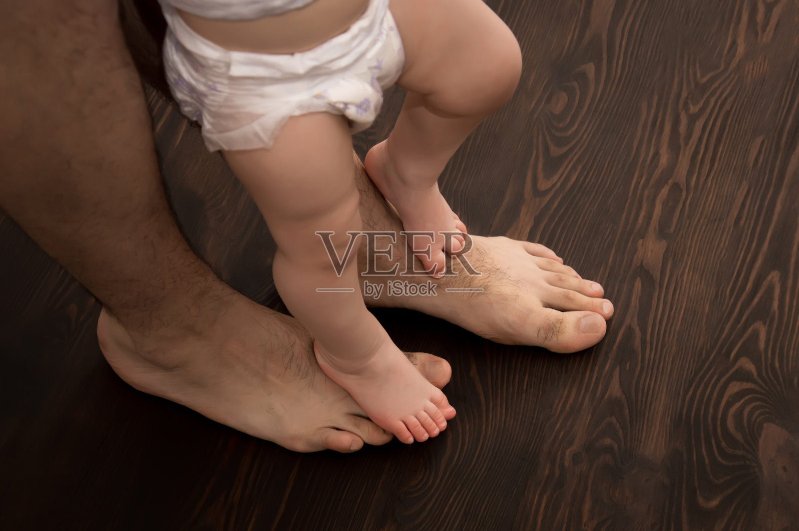 孩子迈出了第一步。雄性的大腿和婴儿的小腿。爸爸帮助孩子迈出第一步。照片摄影图片