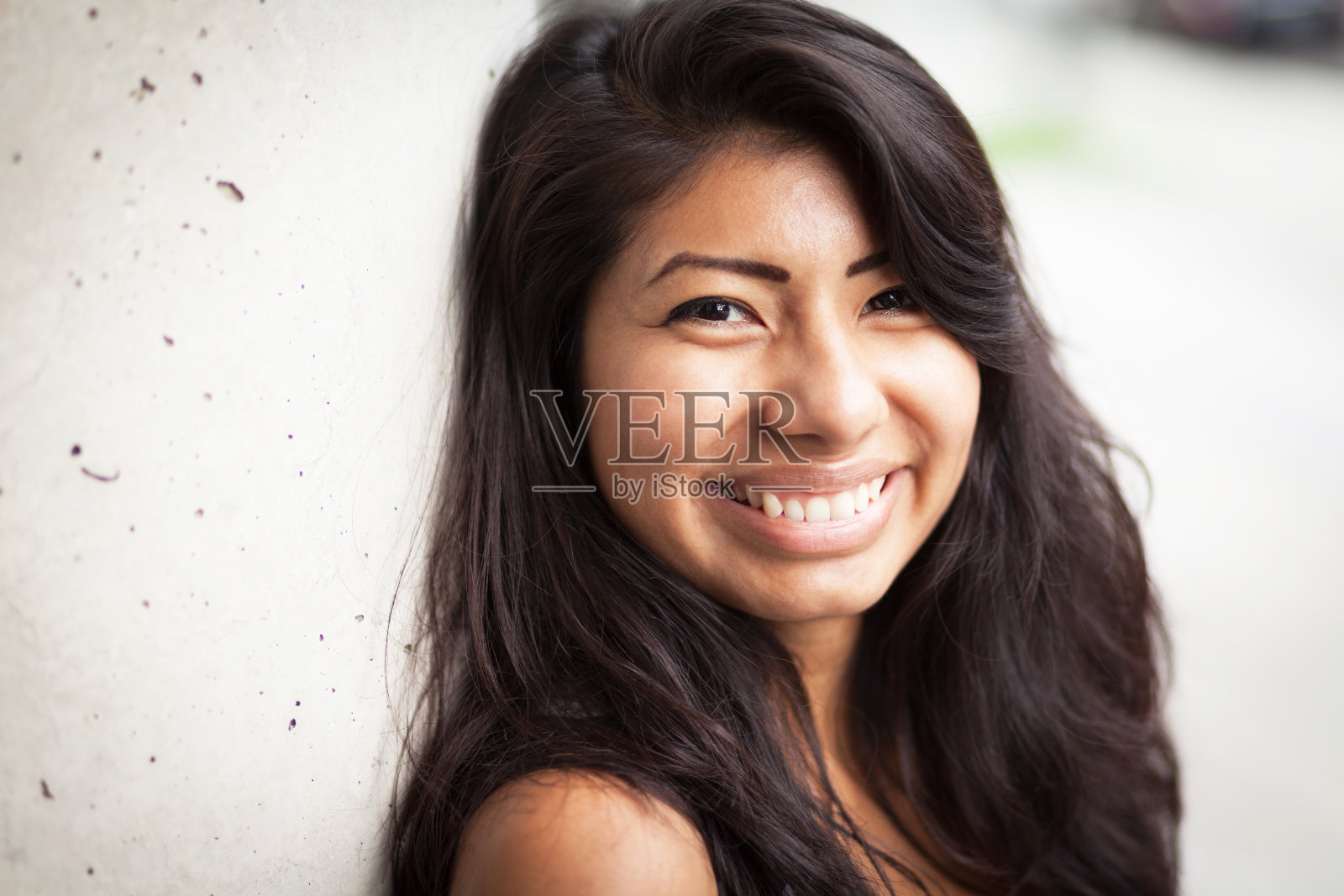年轻的西班牙女人对着镜头微笑。她靠在墙上照片摄影图片