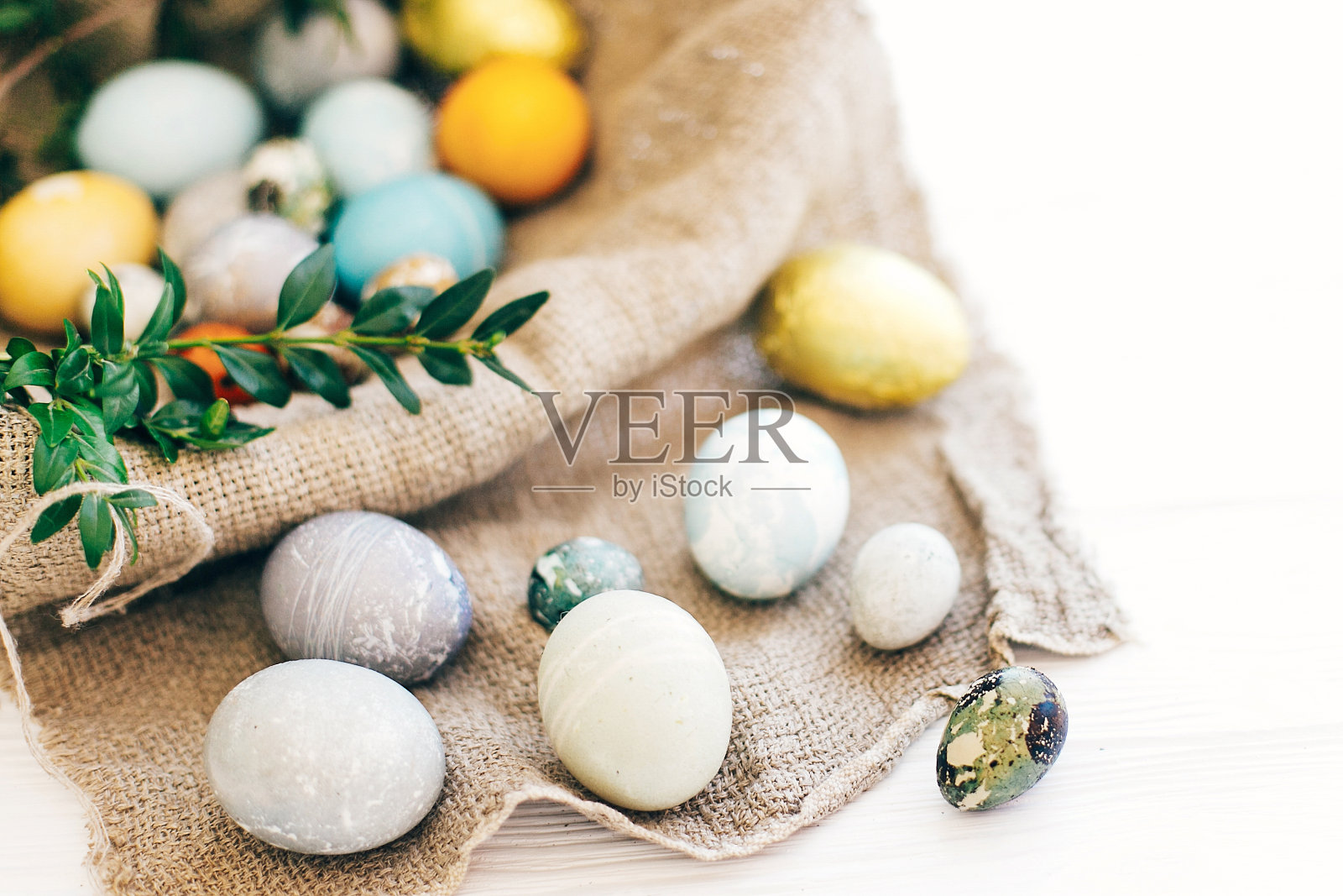 复活节打猎。复活节快乐。时尚的复活节彩蛋和绿色的黄杨树枝在乡村柳条篮子在白色的木制背景。现代金色复活节糖果和鸡蛋涂上天然染料照片摄影图片