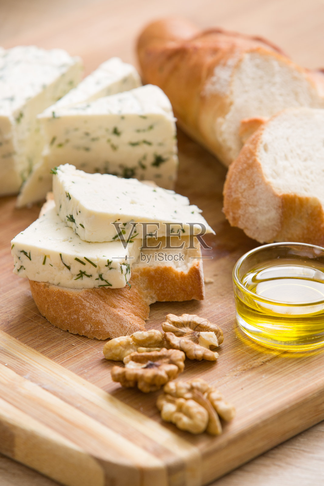 自制奶酪和核桃，橄榄油和面包放在木板上。桌上放着带坚果的咸凝白奶酪。美味的早餐或零食照片摄影图片
