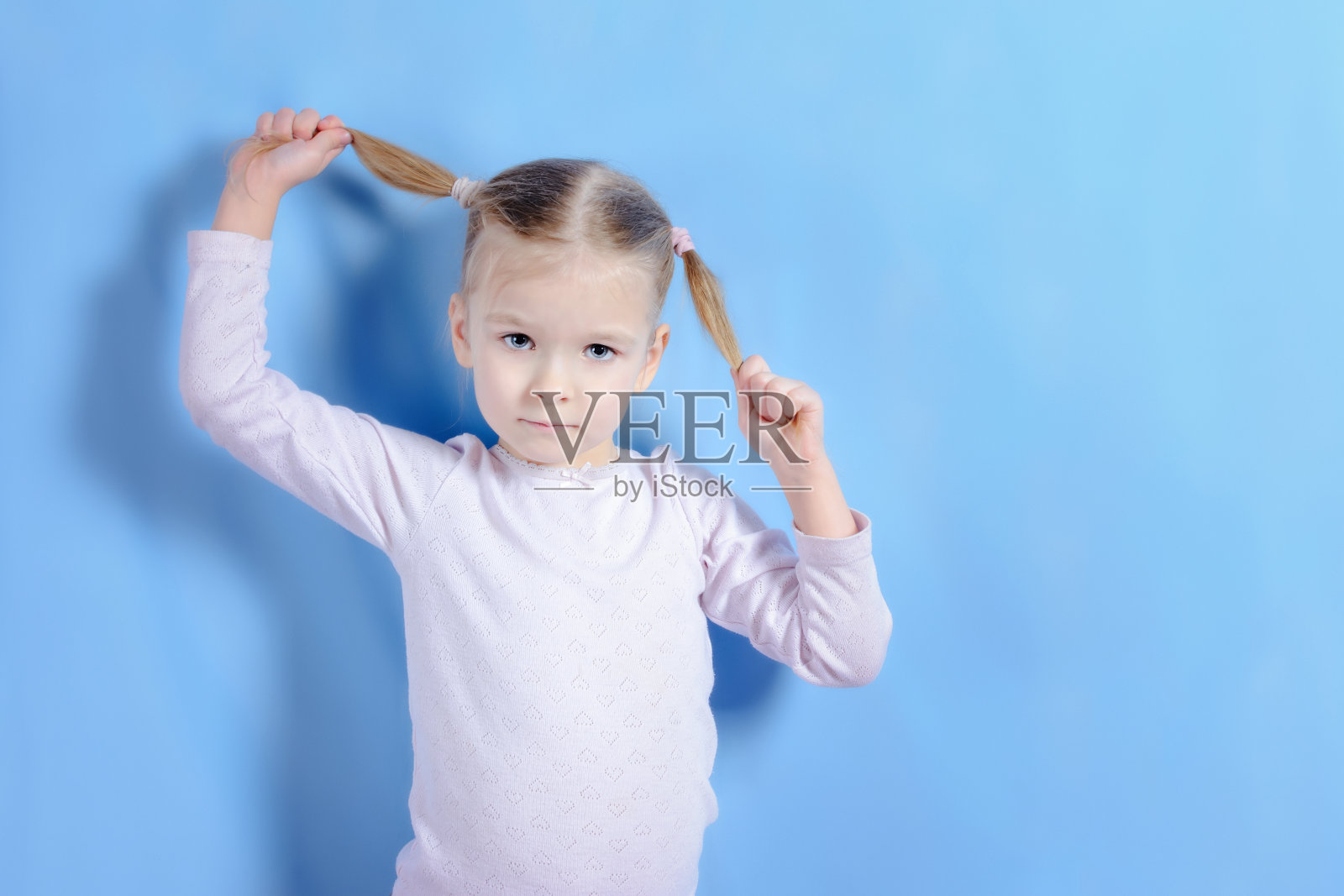 浅色头发和发尾的小女孩。一个漂亮的宝宝玩得很开心。蓝色背景上的照片。照片摄影图片