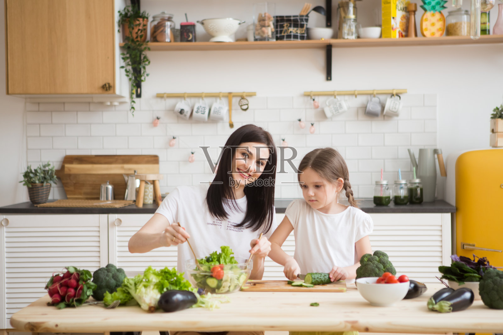 母亲和女儿一起在厨房里准备健康蔬菜沙拉。帮助孩子成为父母。照片摄影图片