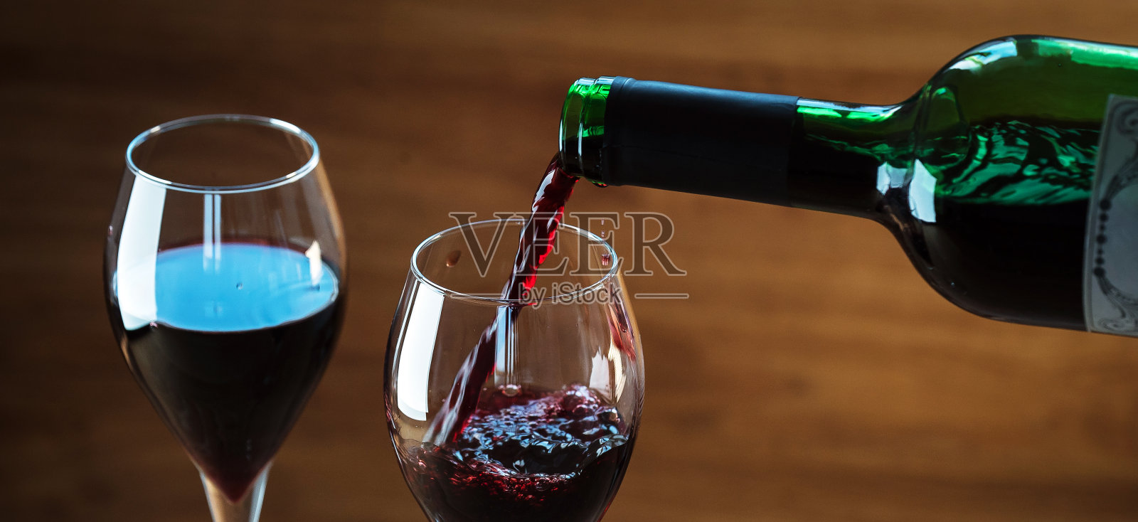 将红酒倒入玻璃杯中，以木色为背景照片摄影图片