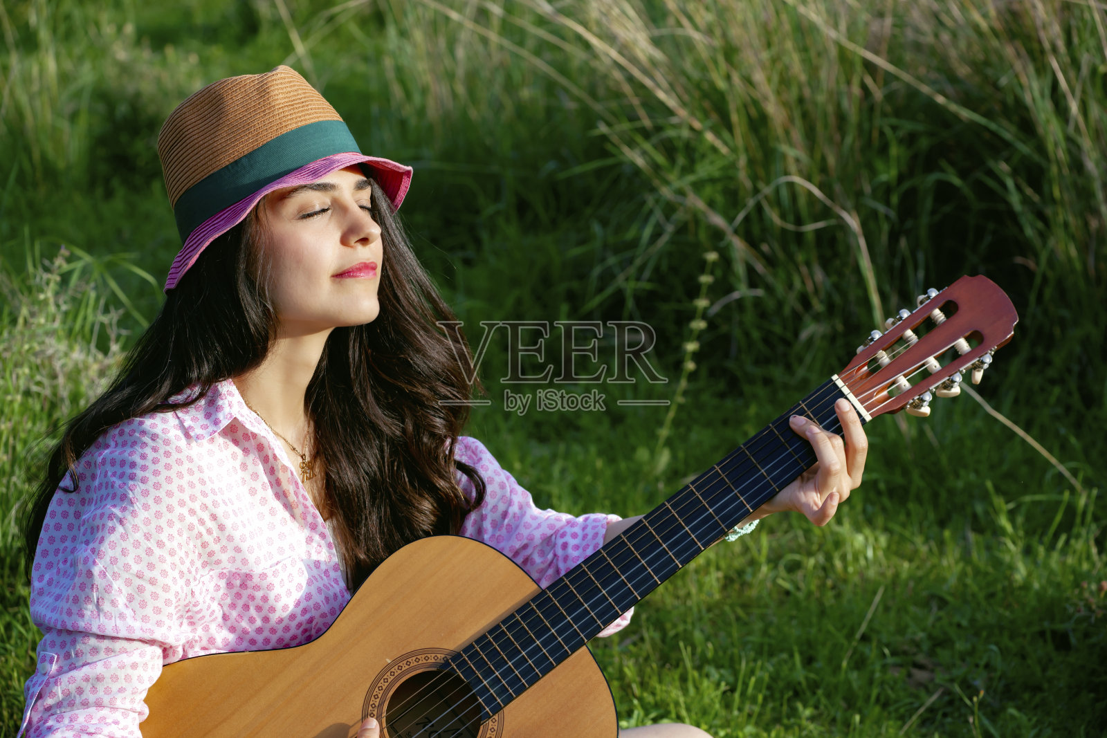 在大自然中抱着吉他弹奏的女孩肖像。照片摄影图片