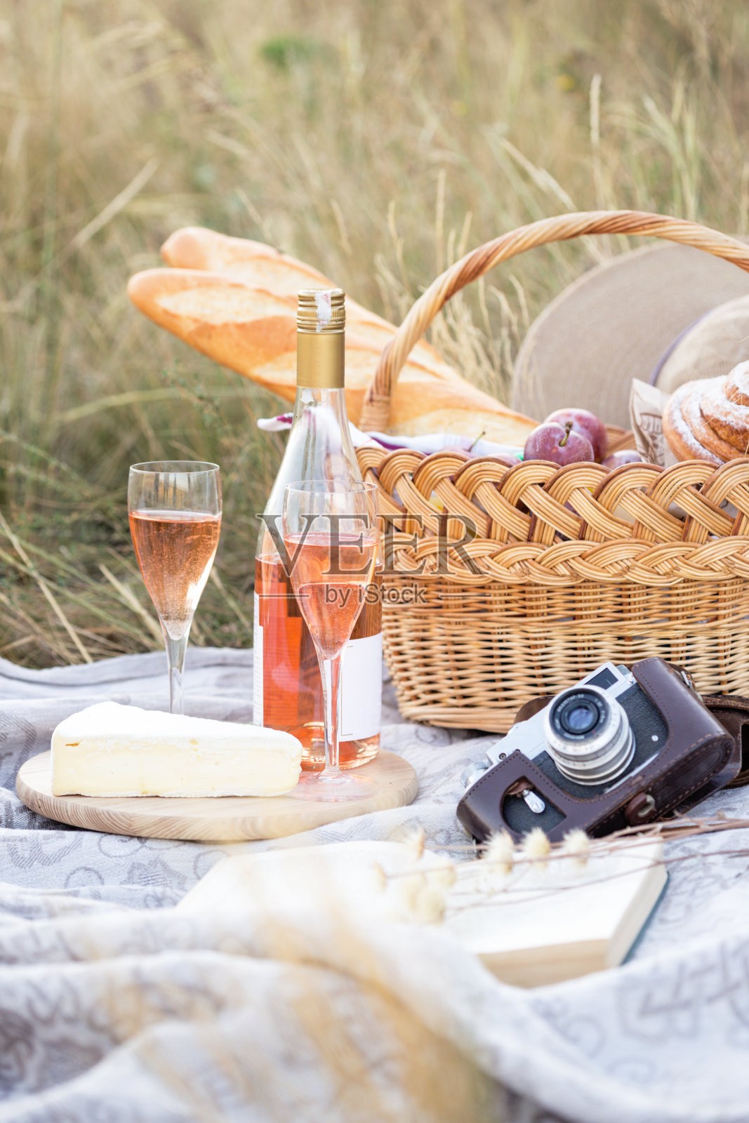 夏天在草地上野餐。拿着篮子去野餐的女孩，里面有法棍面包、葡萄酒、玻璃杯、葡萄和面包卷照片摄影图片