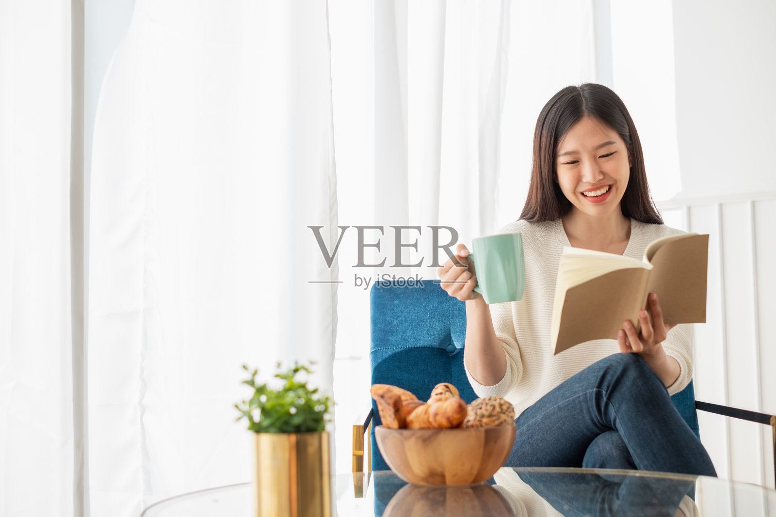 年轻美丽的亚洲女人放松在家里的客厅，阅读书籍，喝咖啡在早上与幸福的感觉照片摄影图片